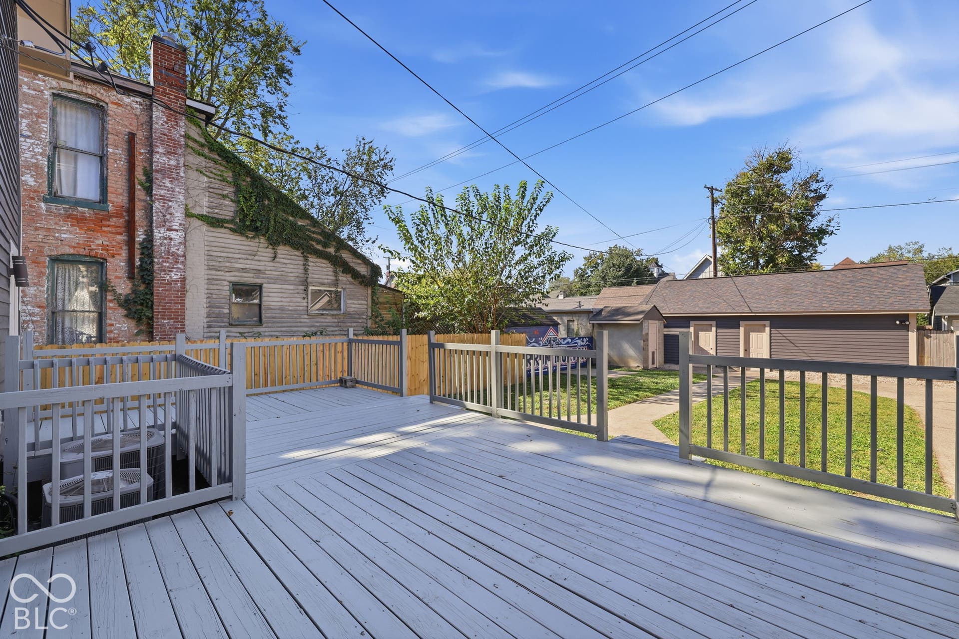 Spacious wood deck with painted railings, leading to a concrete pathway and detached garage structure