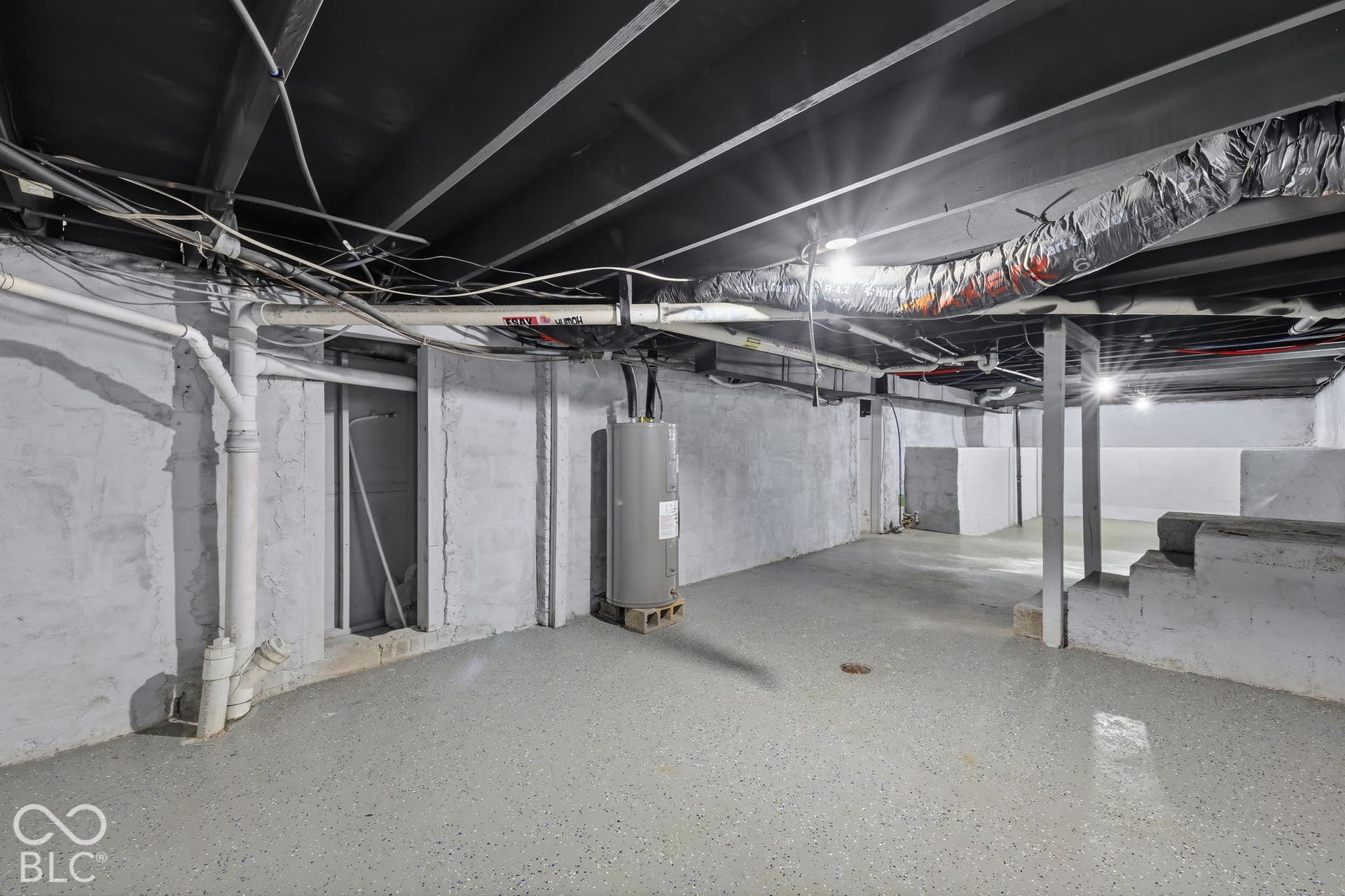 Expansive unfinished basement featuring concrete walls and flooring, exposed ceiling joists, and a water heater