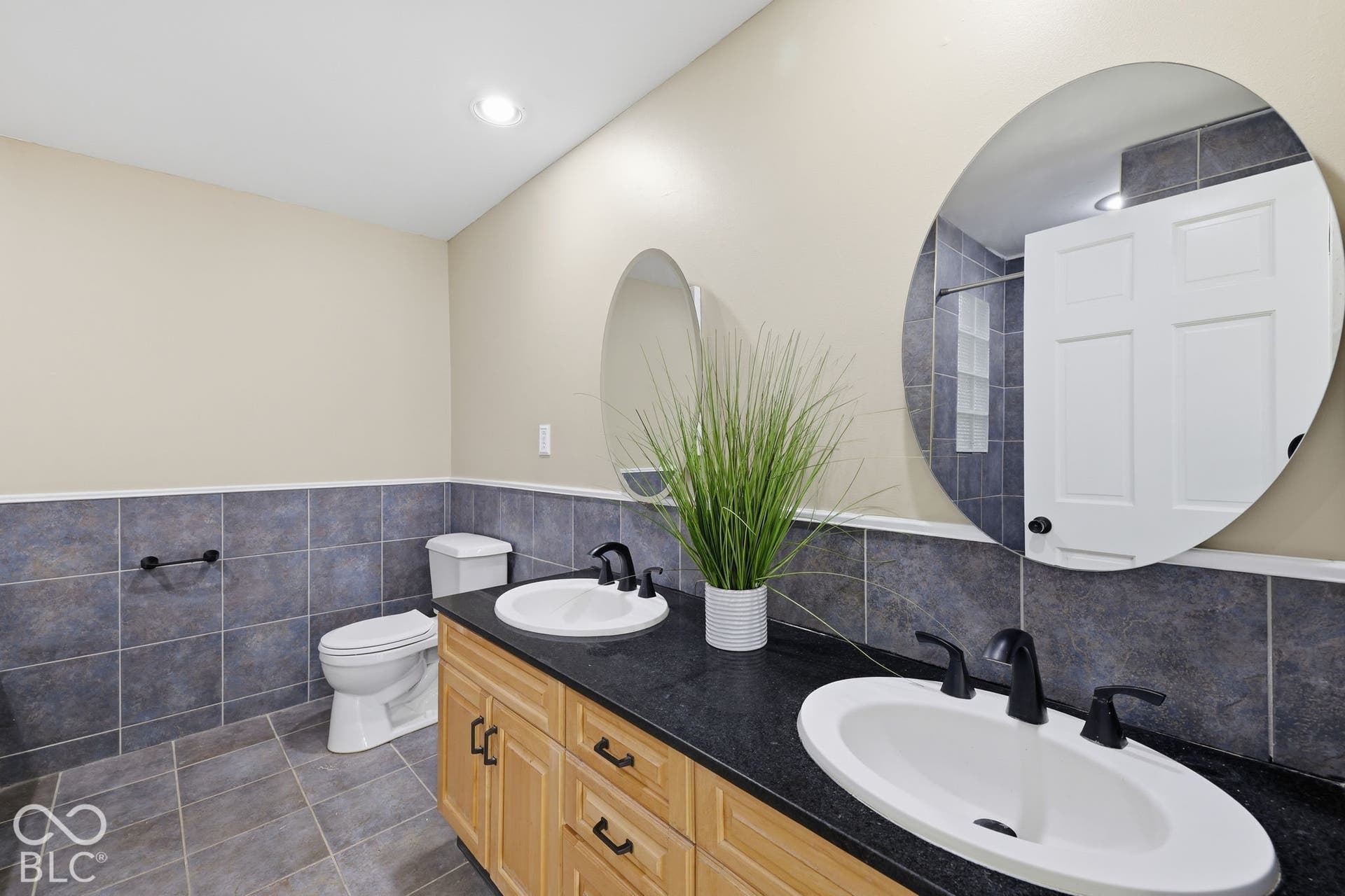 Double vanity with black countertop and undermount sinks, natural wood-finish cabinetry, and matte black fixtures