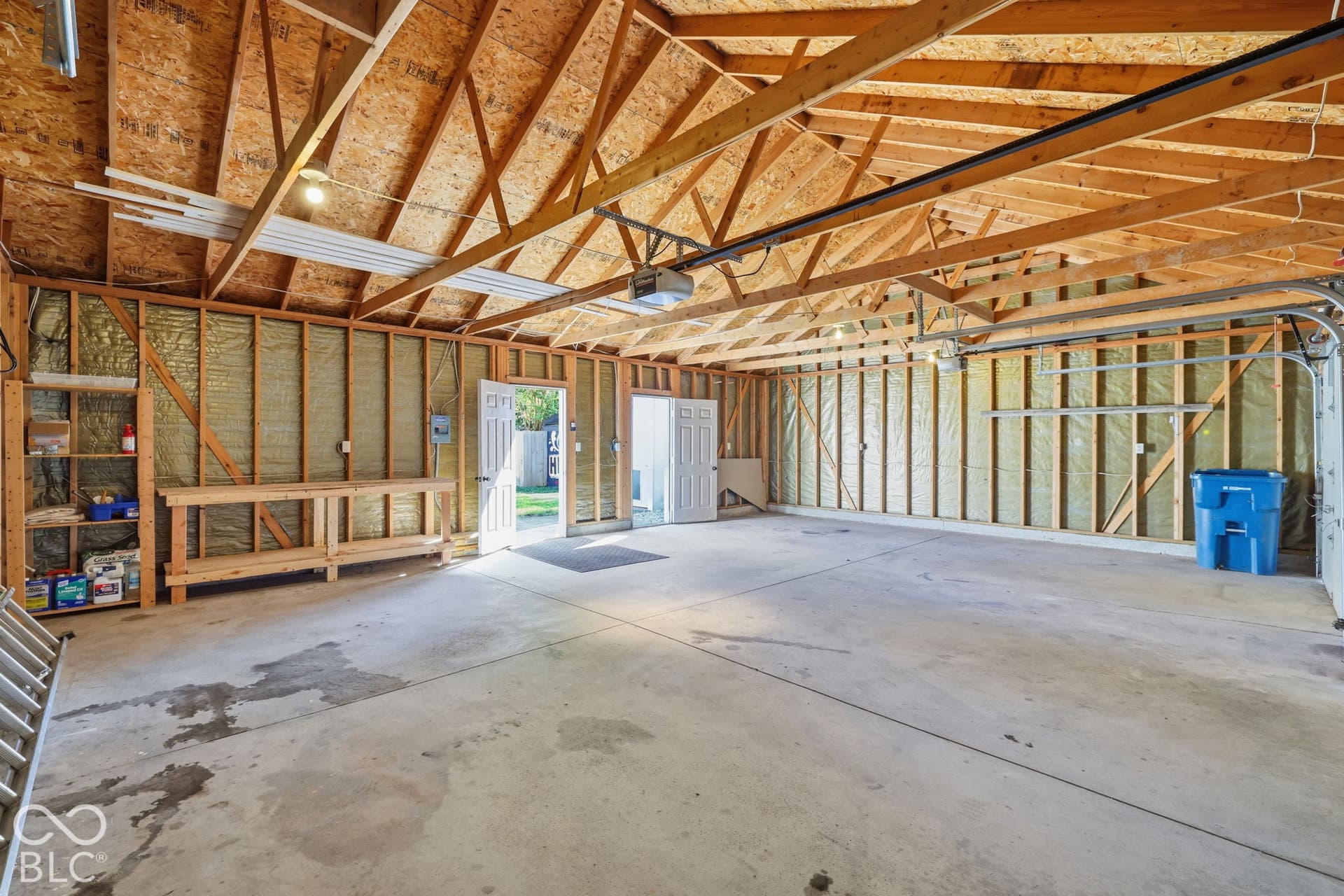 Spacious garage featuring exposed wood rafters, concrete flooring, built-in shelving, and a workbench