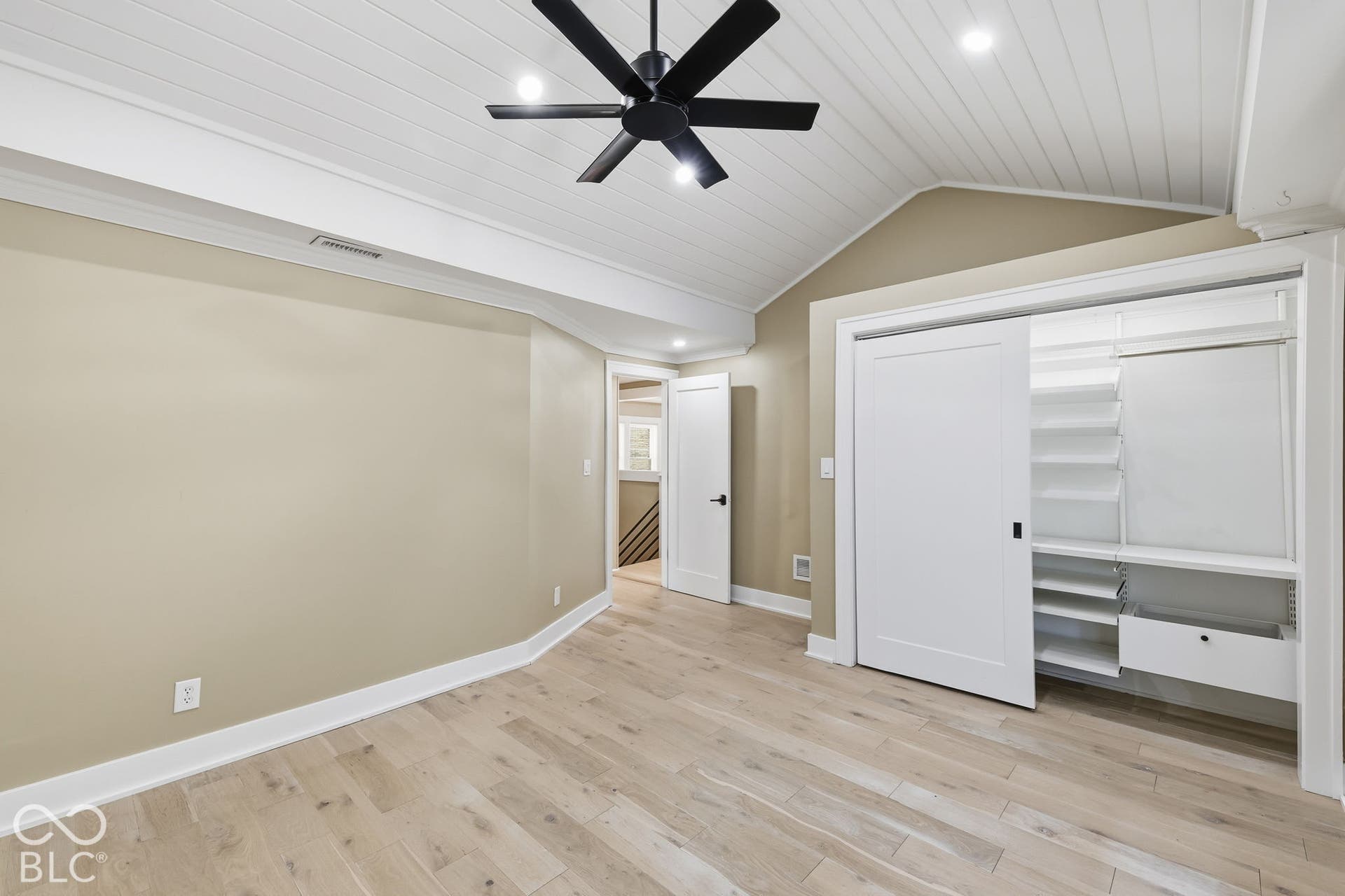 Light wood-finish flooring with a white trim, sloped planked ceiling with recessed lighting, and a black ceiling fan