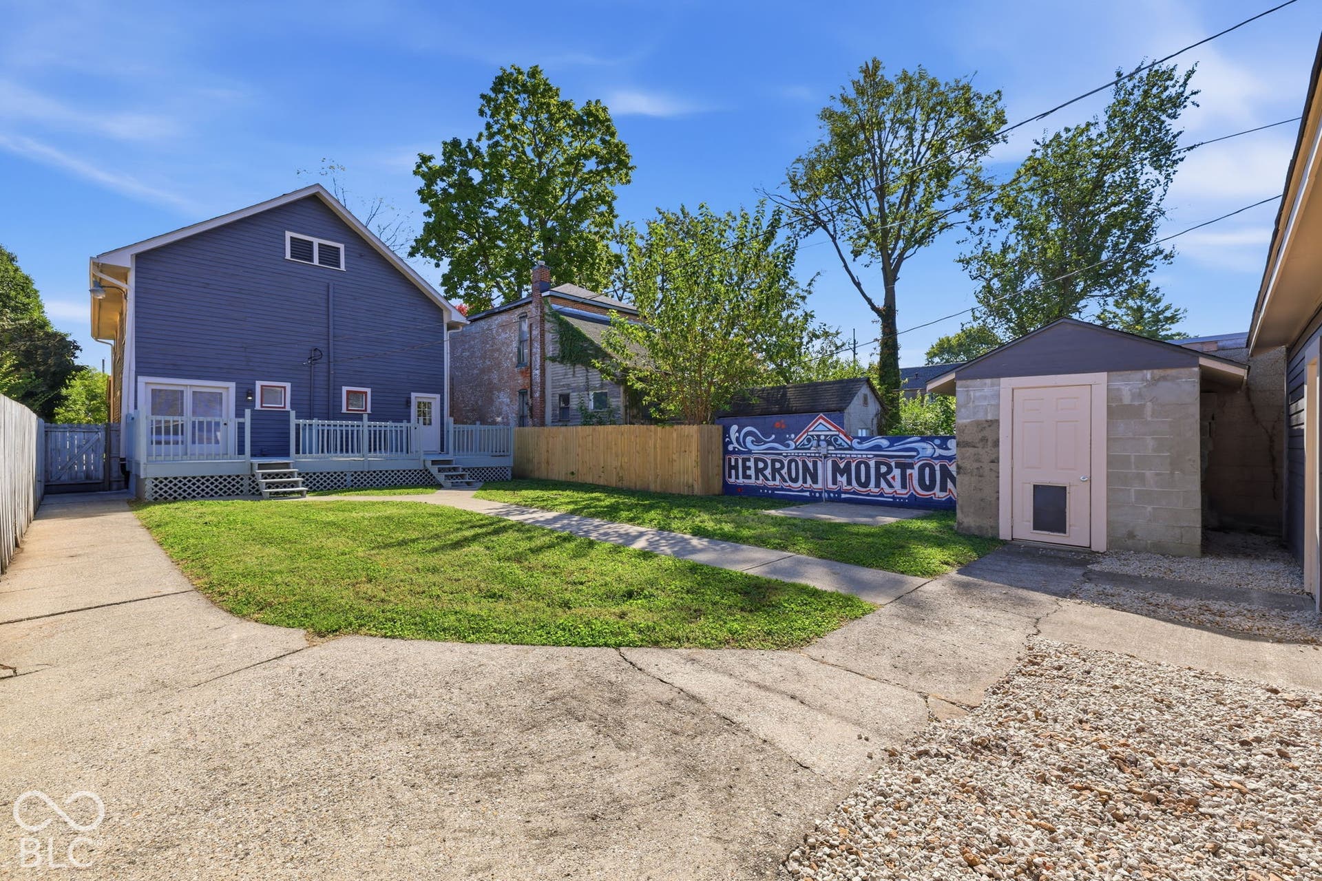 Blue siding exterior, expansive rear deck with railings, concrete driveway, and detached storage structure