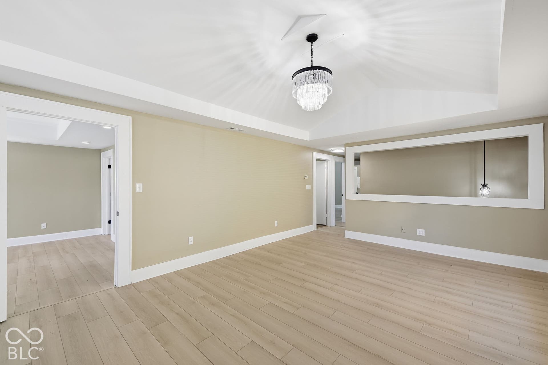 Tray ceiling with a decorative chandelier, light wood-finish flooring, and white trim throughout
