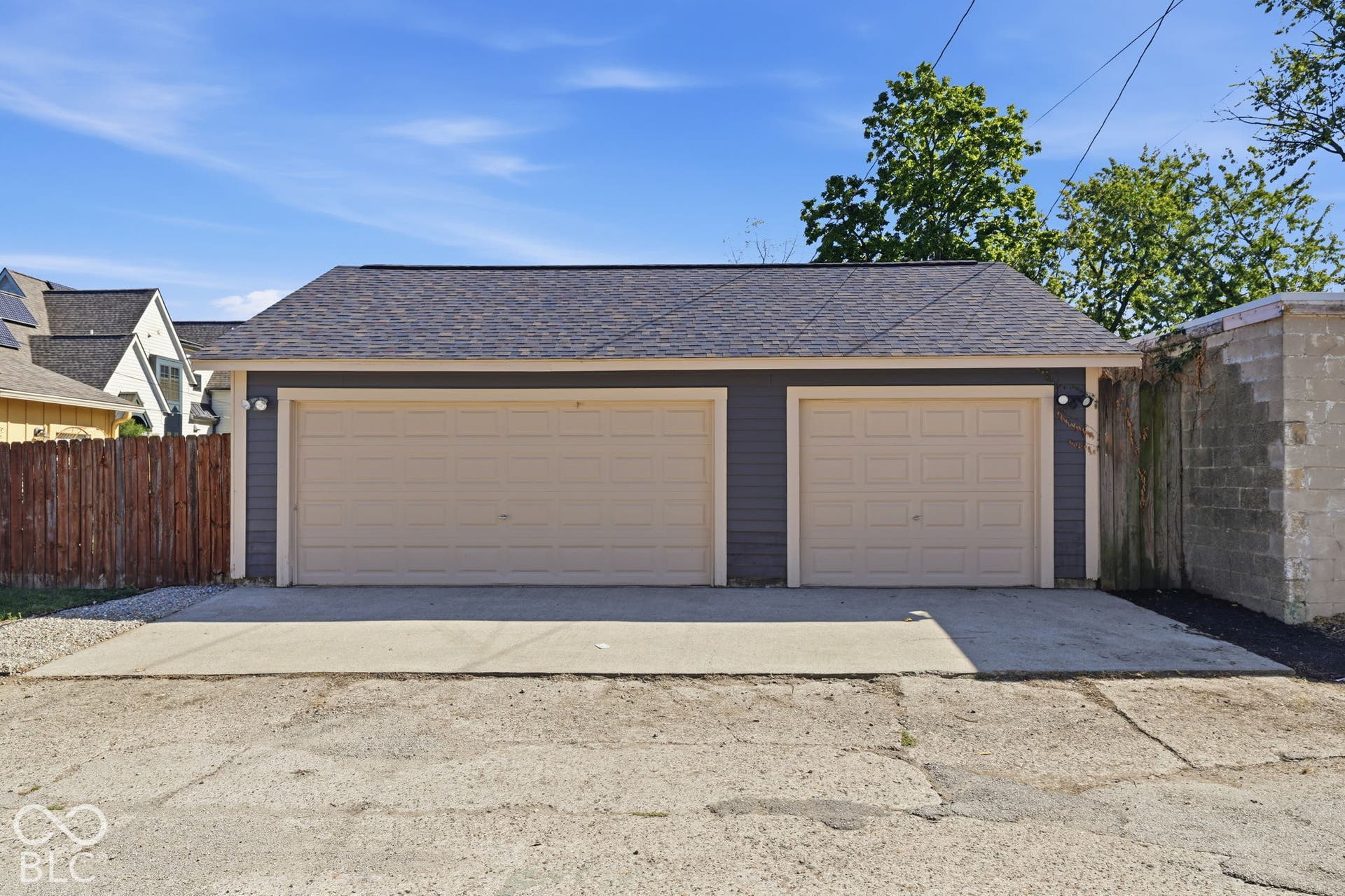 Detached garage featuring two garage doors, dark gray siding, an asphalt shingle roof, and exterior lighting