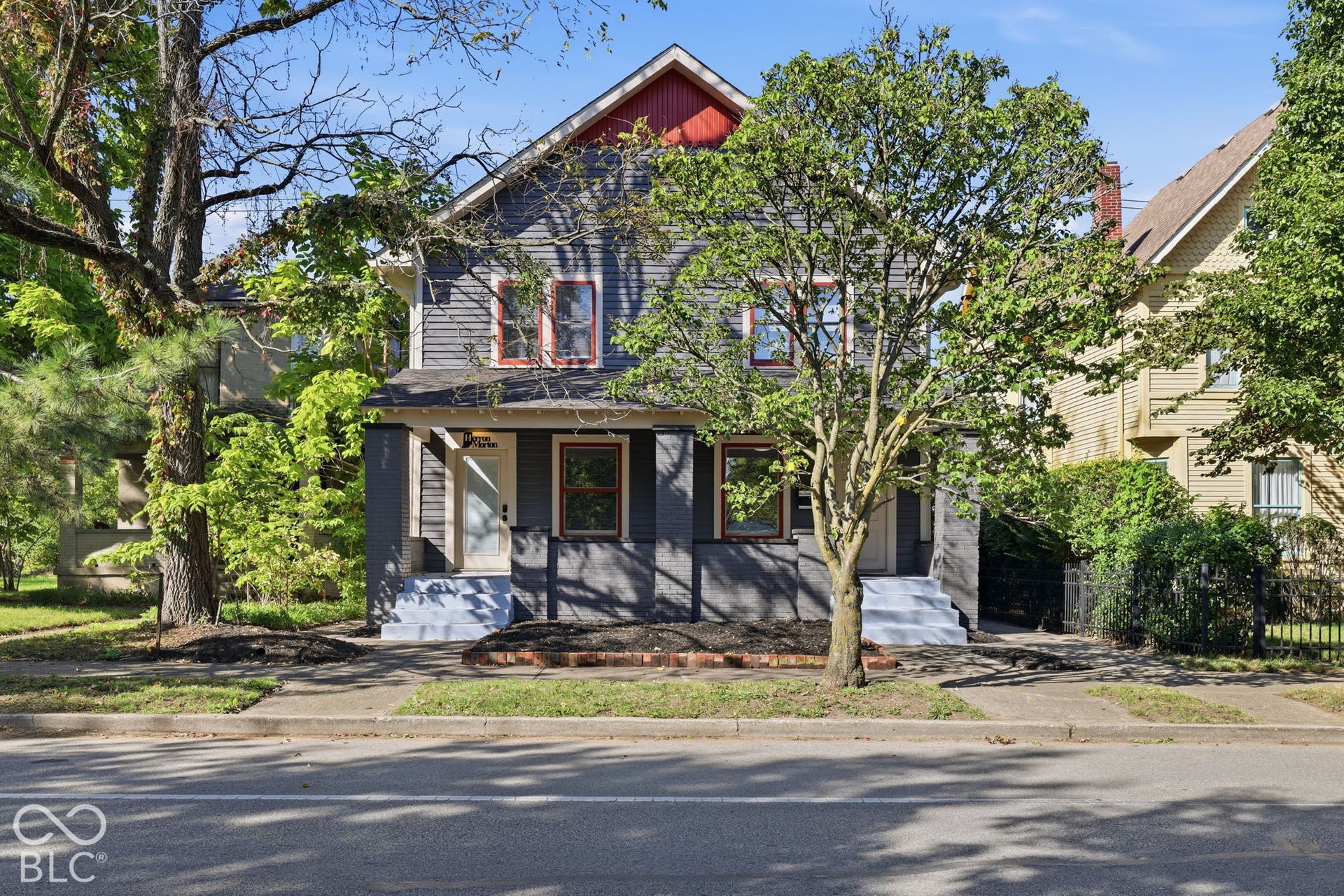 Two-story residence featuring grey siding, red trim accents, a prominent gable roof, and a covered front porch with white steps