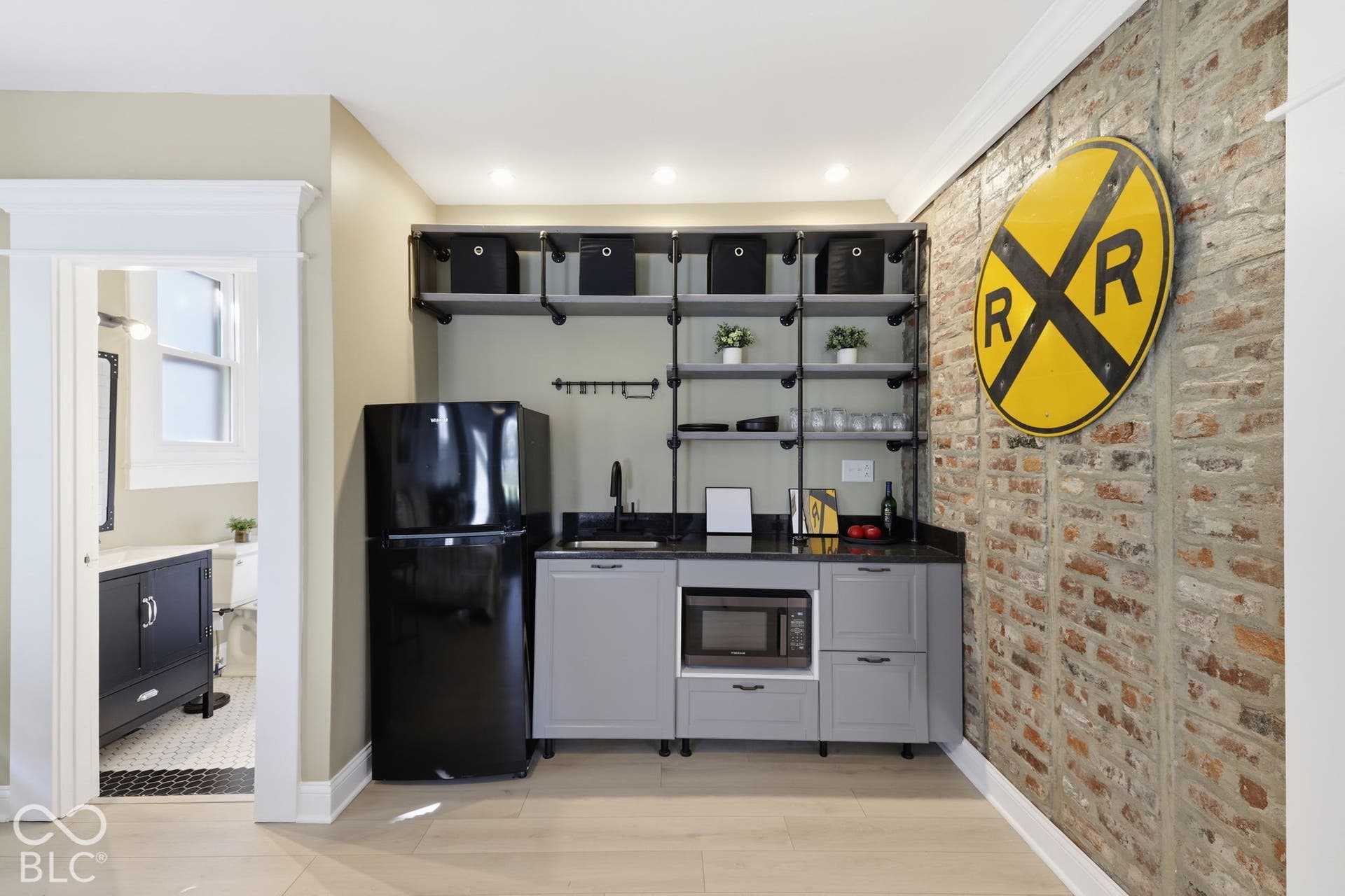 Compact kitchenette featuring an exposed brick accent wall, light wood-finish flooring, and open shelving