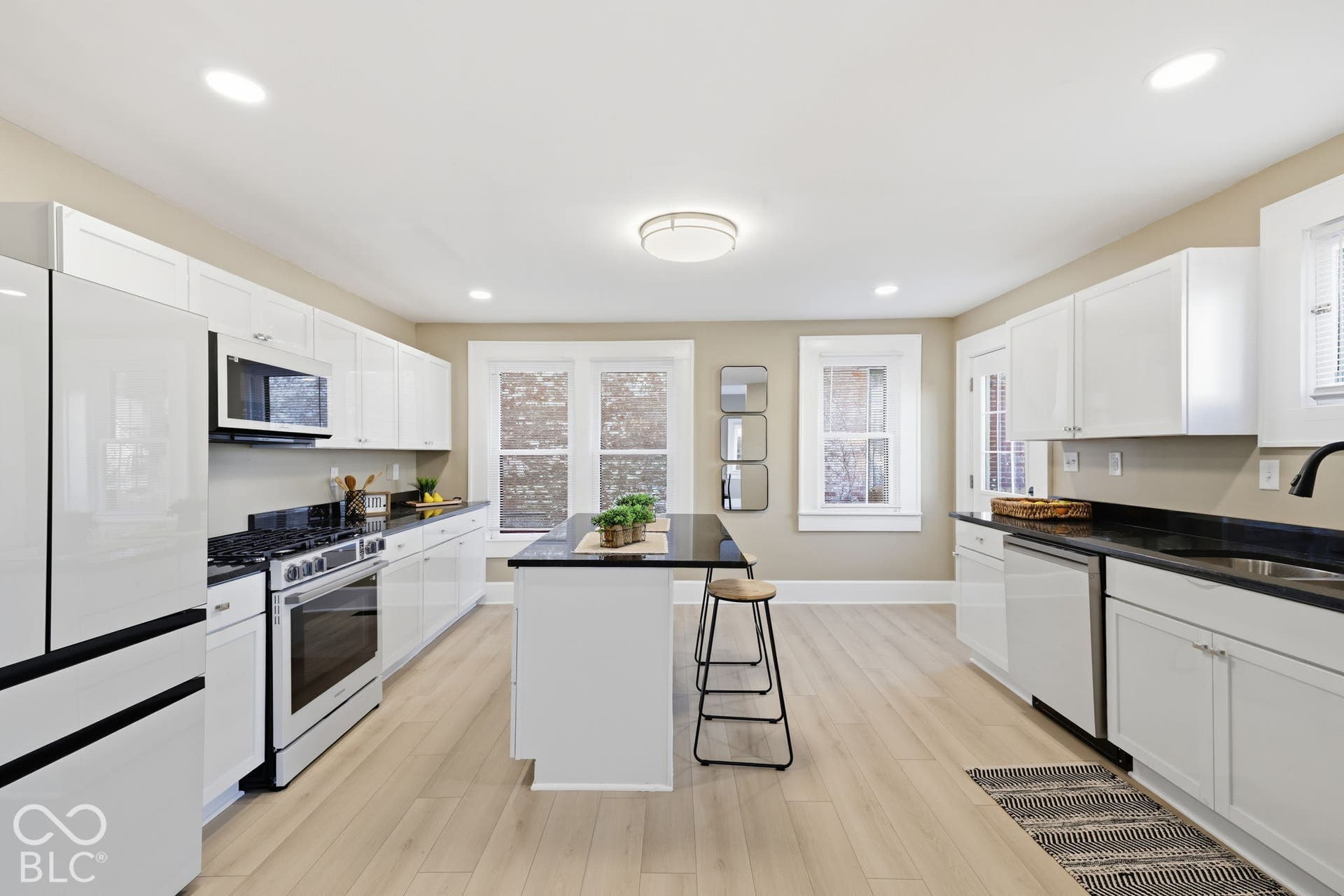 Kitchen featuring wood-finish flooring, white cabinetry, black countertops, and a central island