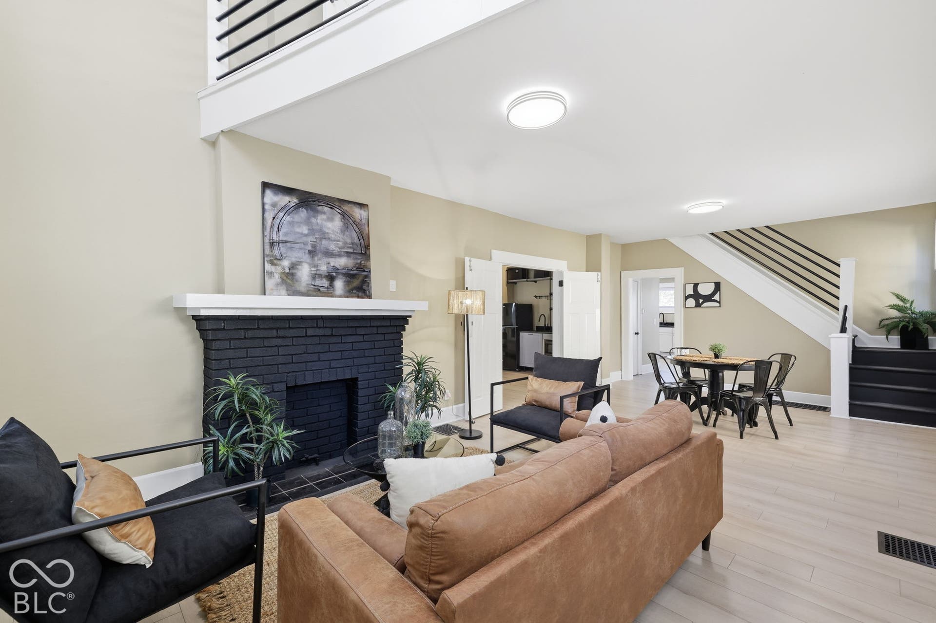 Open concept living area featuring a black brick fireplace with a white mantel, light wood-finish flooring, and a staircase with black railings