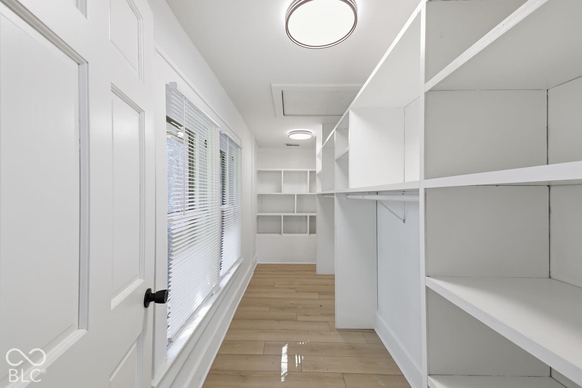 Expansive built-in shelving, integrated hanging rods, flush-mount lighting, wood-finish flooring, and multiple windows with blinds