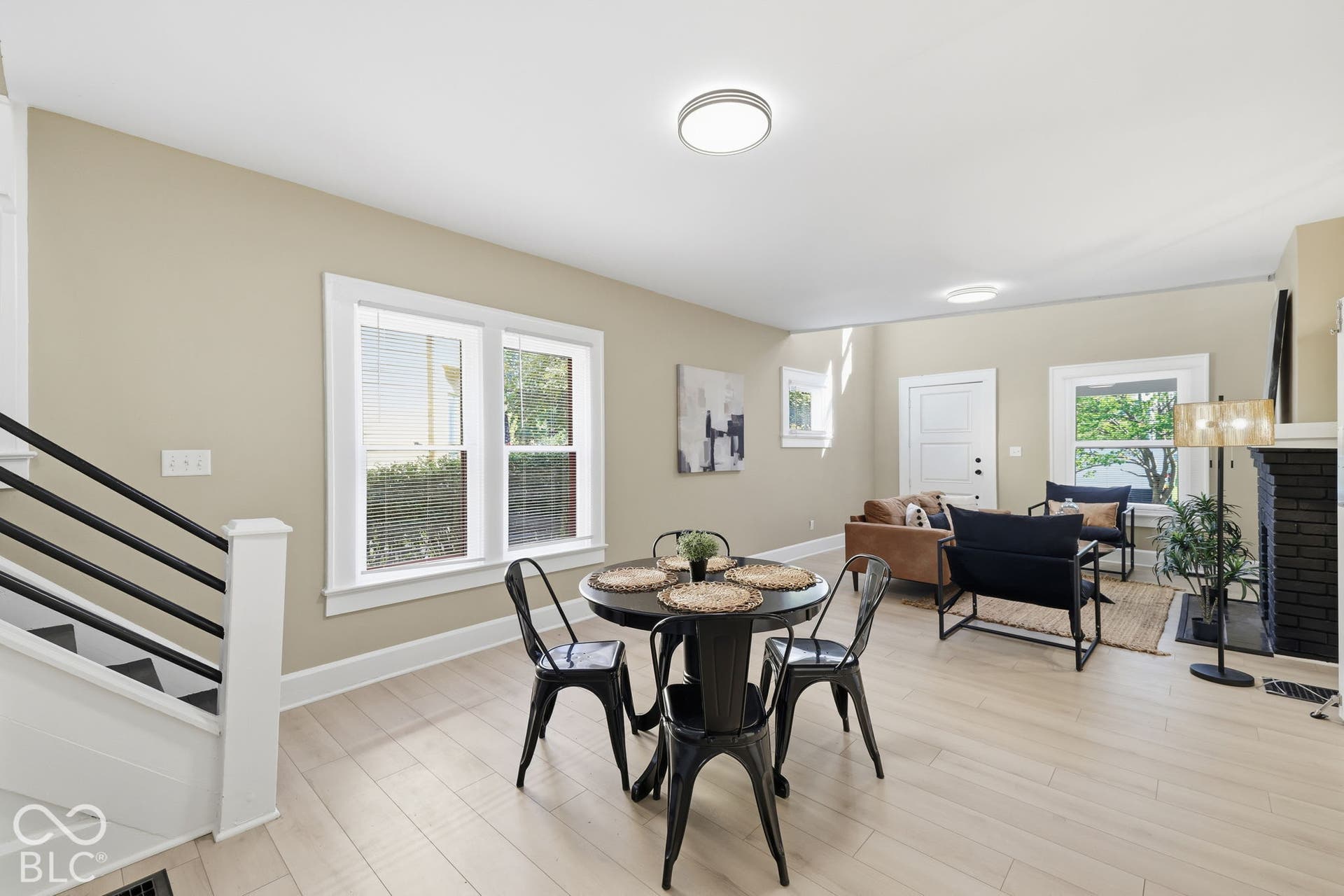 Open-concept living space with light wood-finish flooring, multiple windows, and a black brick fireplace