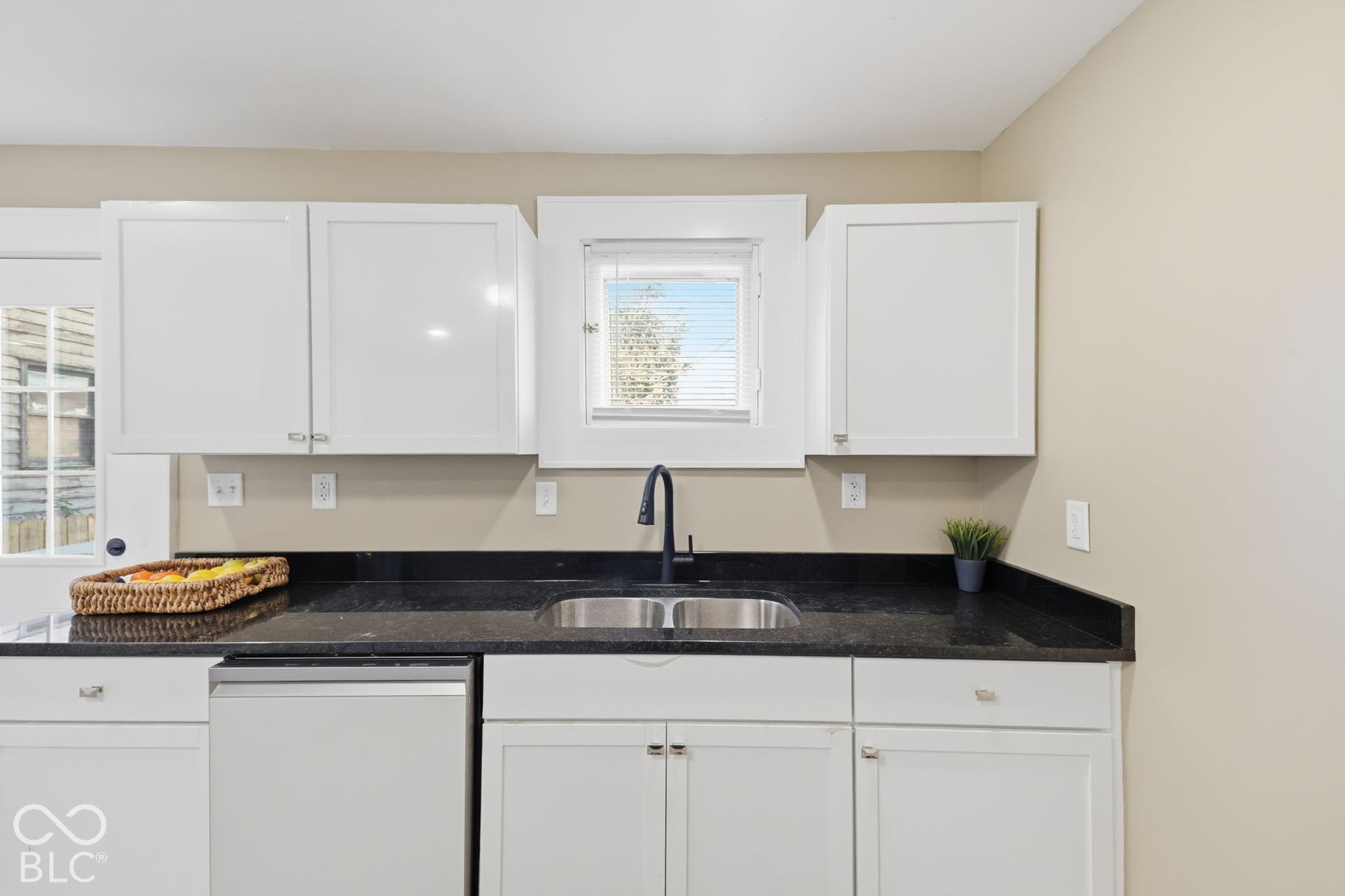 White shaker cabinetry, dark countertops, stainless steel double basin sink, and a black gooseneck faucet