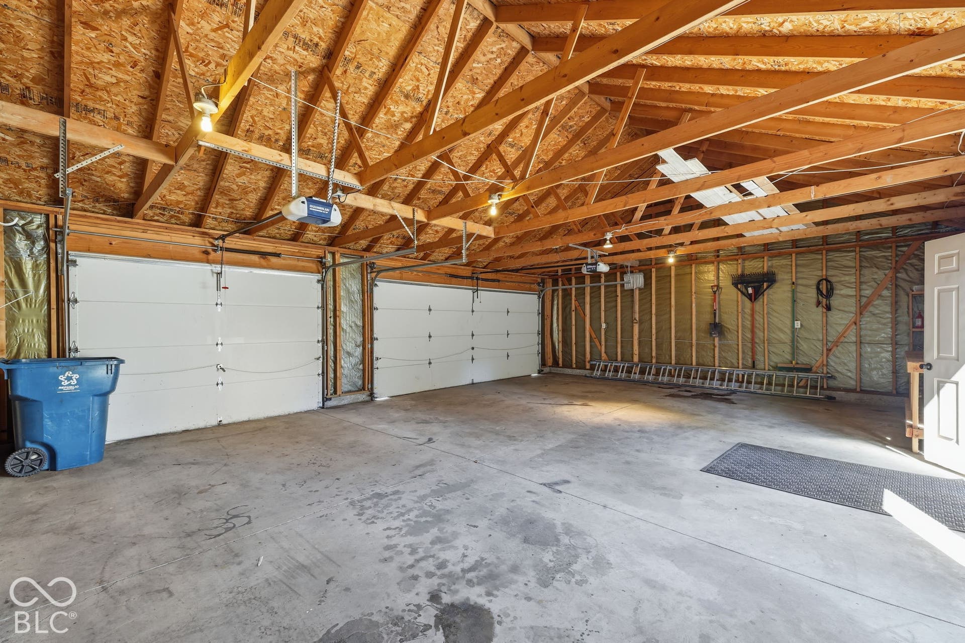 Expansive garage featuring multiple automatic overhead doors, exposed wood framing, and overhead lighting