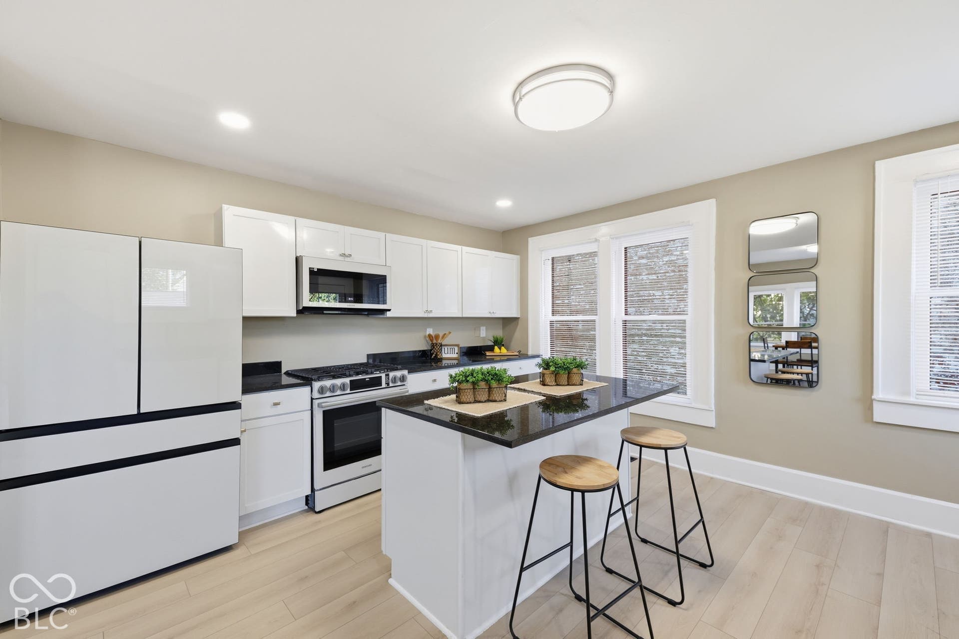 White cabinetry, black countertops, stainless steel appliances, central island, and light wood-finish flooring