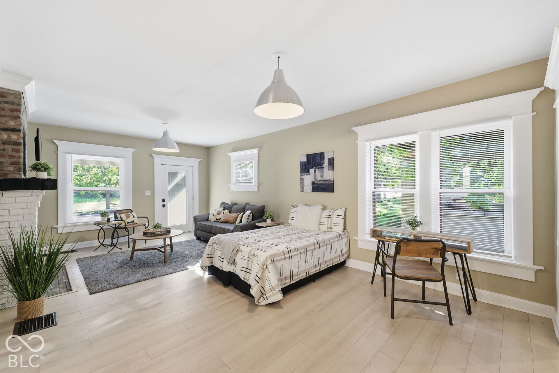 Light wood-finish flooring, white brick fireplace with brick detailing, white trim windows, white interior door with glass panel, and two pendant light fixtures