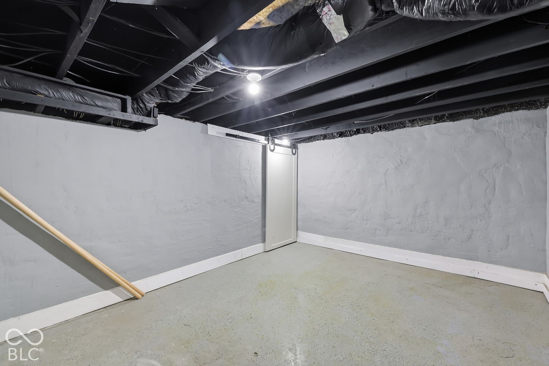 Painted concrete walls with white trim, exposed black ceiling joists, and a barn door leading to an interior space