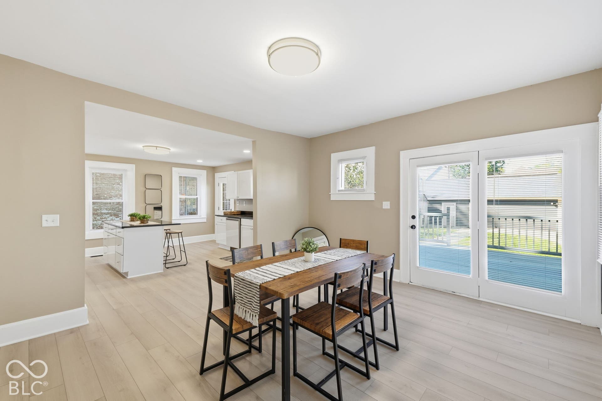 Light wood-finish flooring throughout, neutral wall paint, white trim, and a rectangular opening to the kitchen