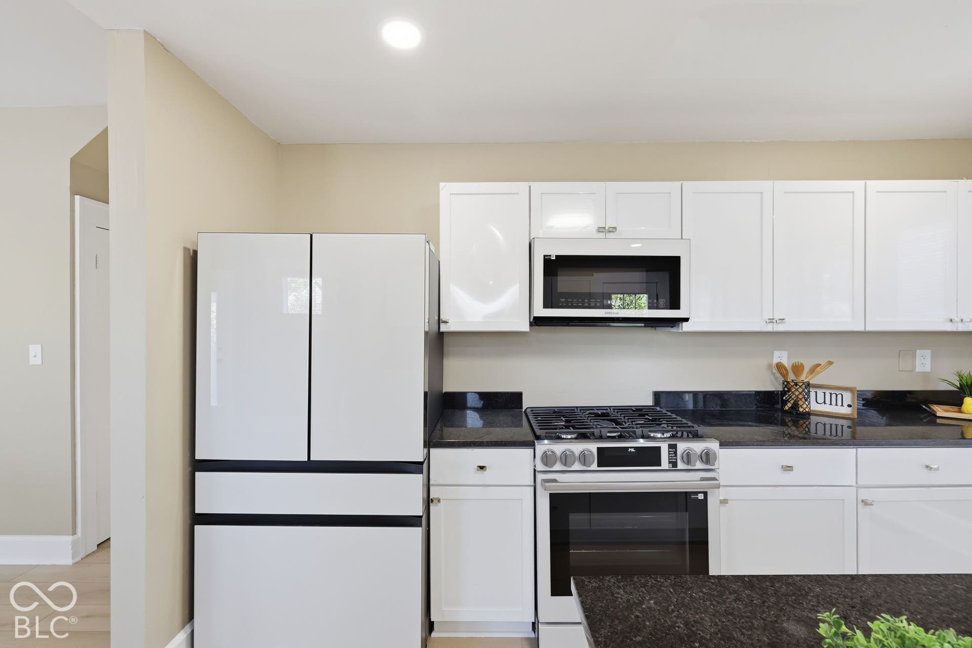 White cabinetry with silver-tone hardware, stainless steel gas range with oven, built-in microwave, and dark-toned countertops