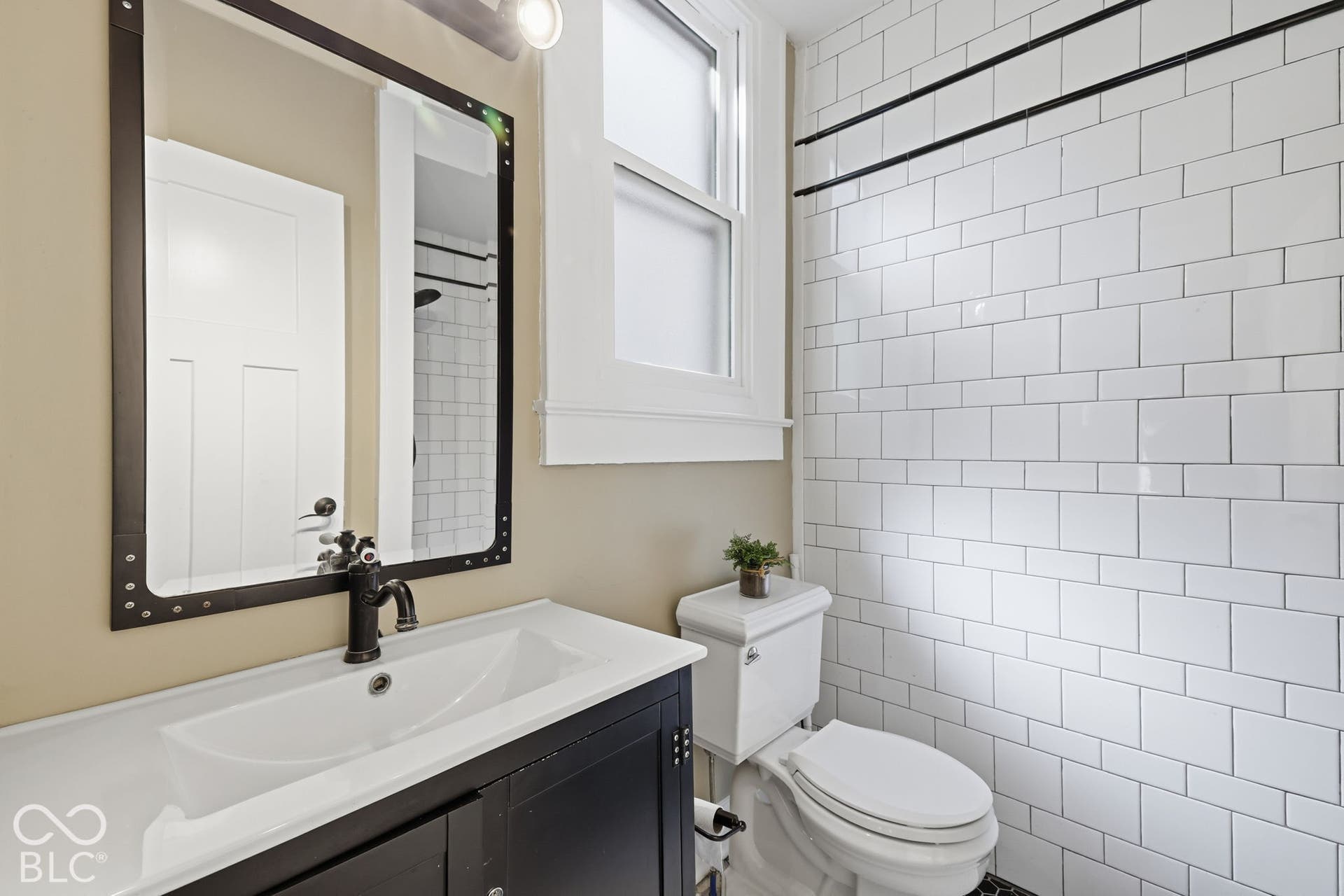 White subway tile shower surround, dark wood-finish vanity with an integrated sink, black metal-framed mirror, and a white toilet