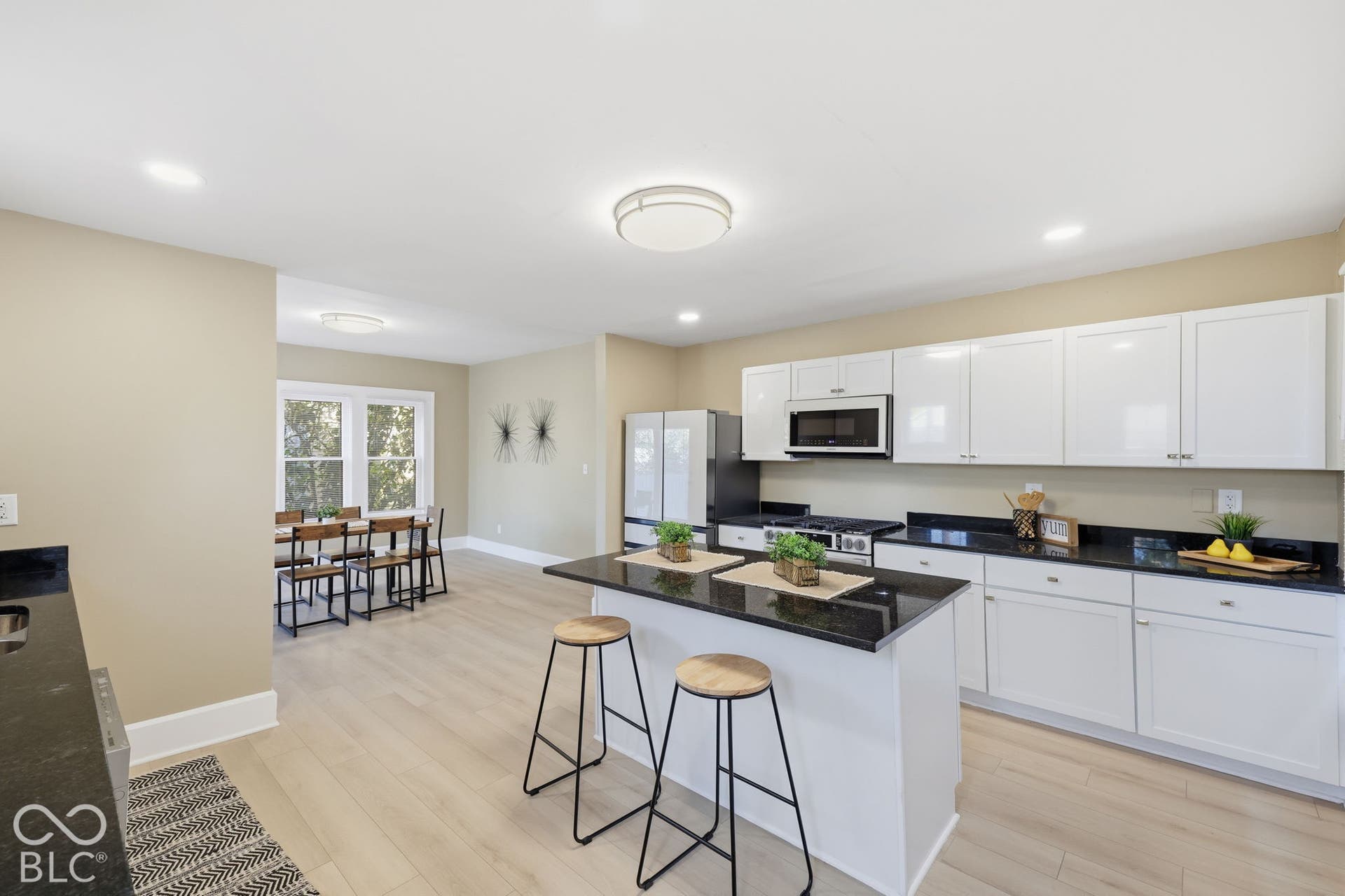 Recessed lighting, wood-finish flooring, white cabinetry, dark stone countertops, and a kitchen island with seating