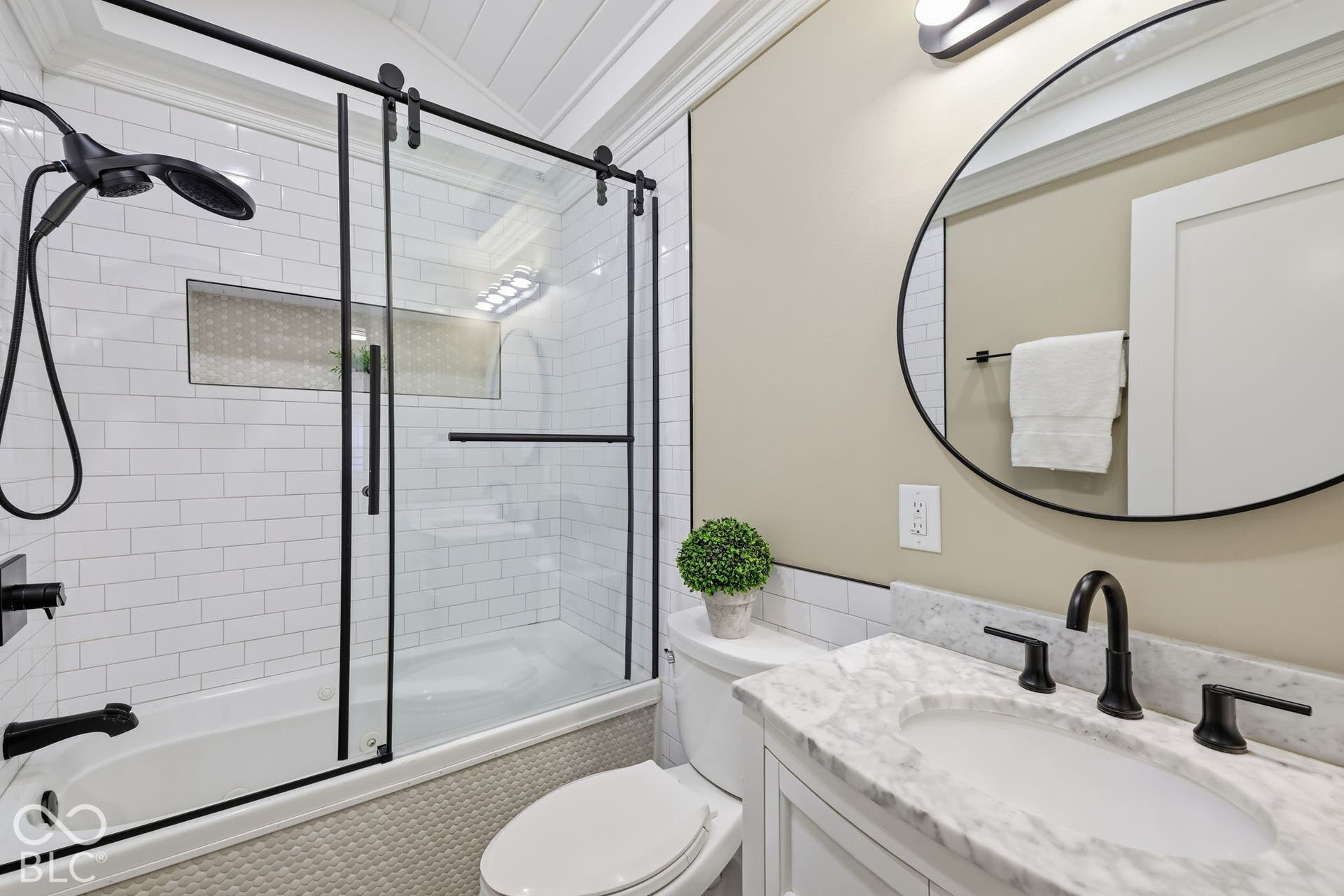 Tub and shower combination with black-framed glass sliding doors, white subway tile surround, and matte black fixtures