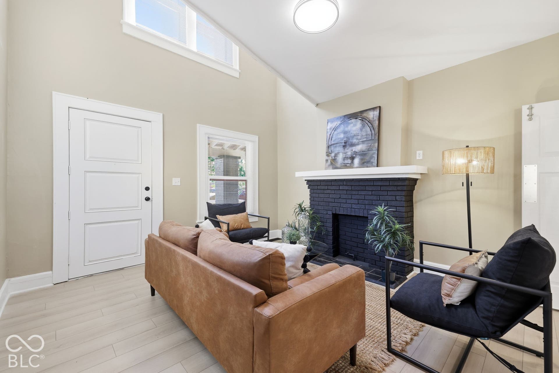 Vaulted ceiling with transom windows, wood-finish flooring, and a brick fireplace with a white mantel