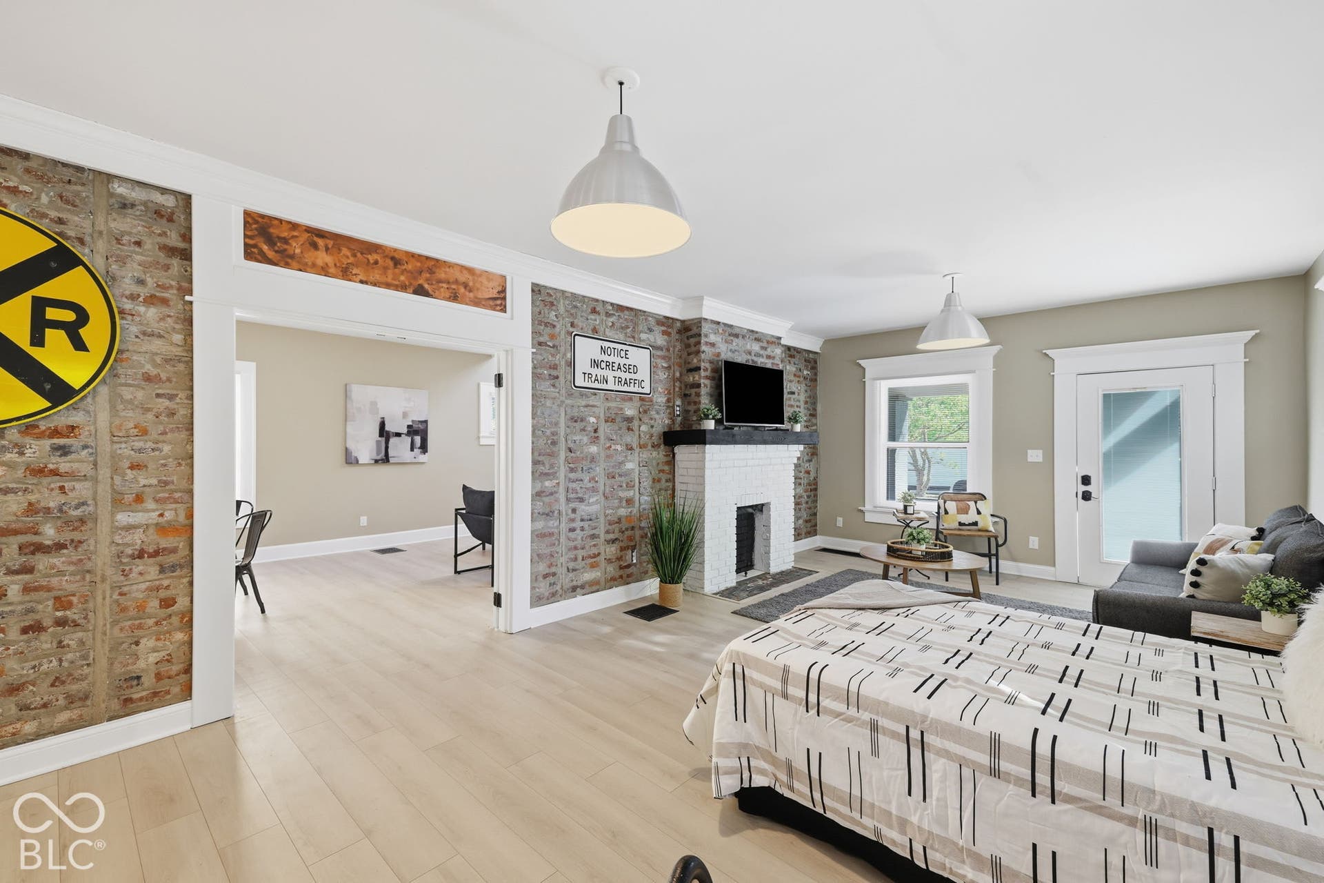 Light wood-finish flooring, exposed brick accents, white-painted brick fireplace, pendant lighting, and crisp white trim