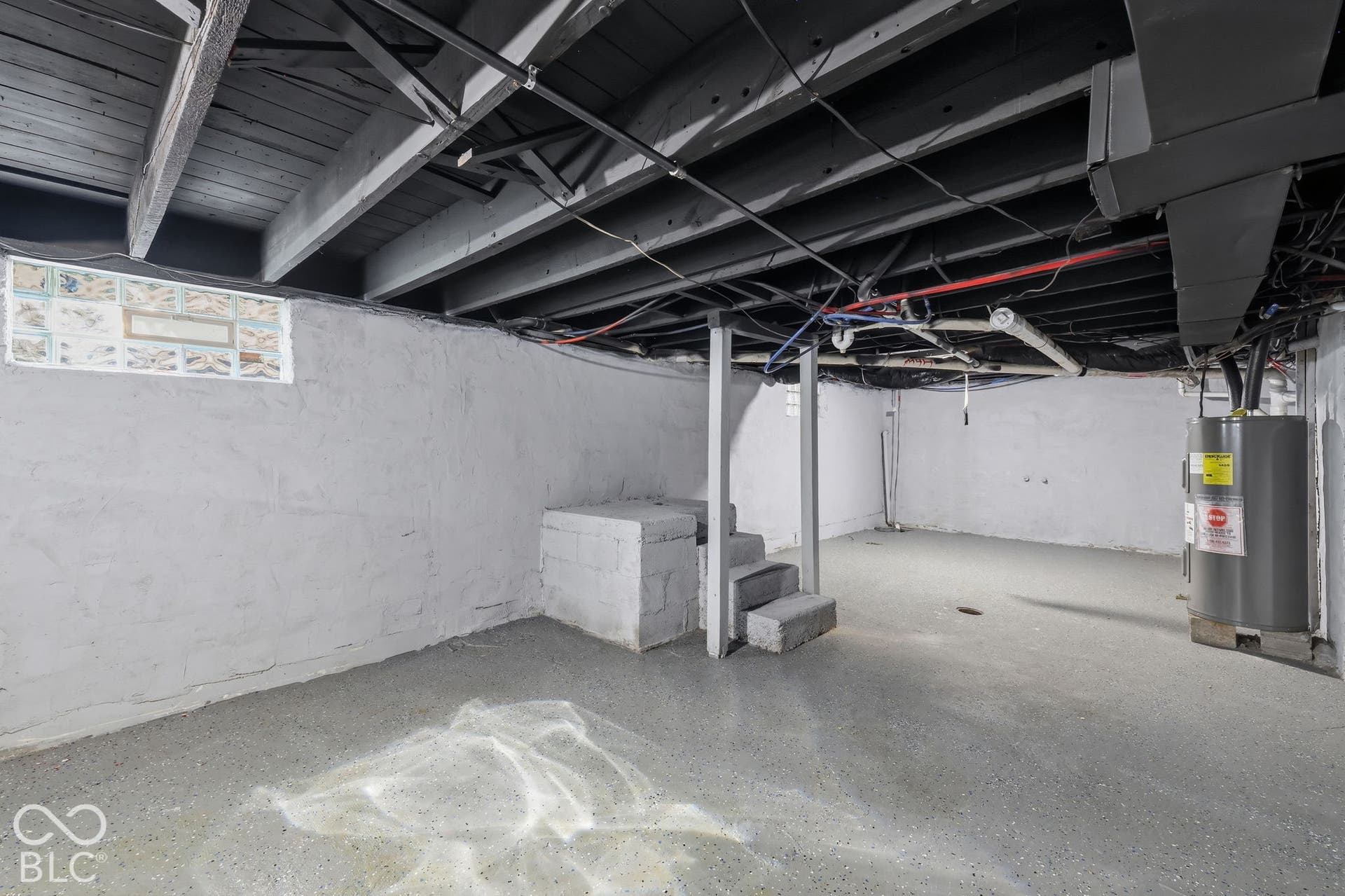 Unfinished basement featuring exposed joists, concrete block walls, and a water heater