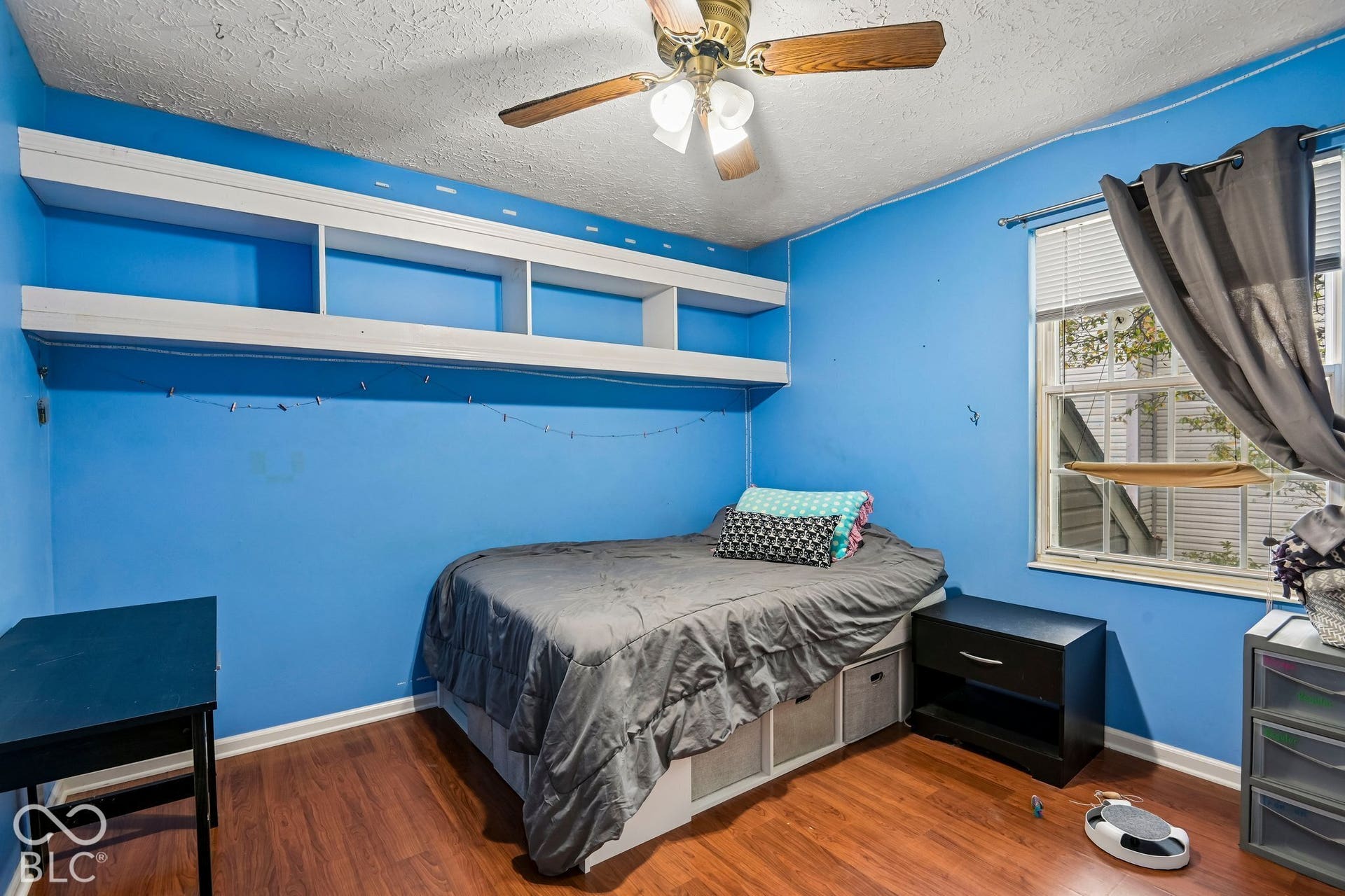 Wood-finish flooring, built-in shelving, ceiling fan, and window with blinds