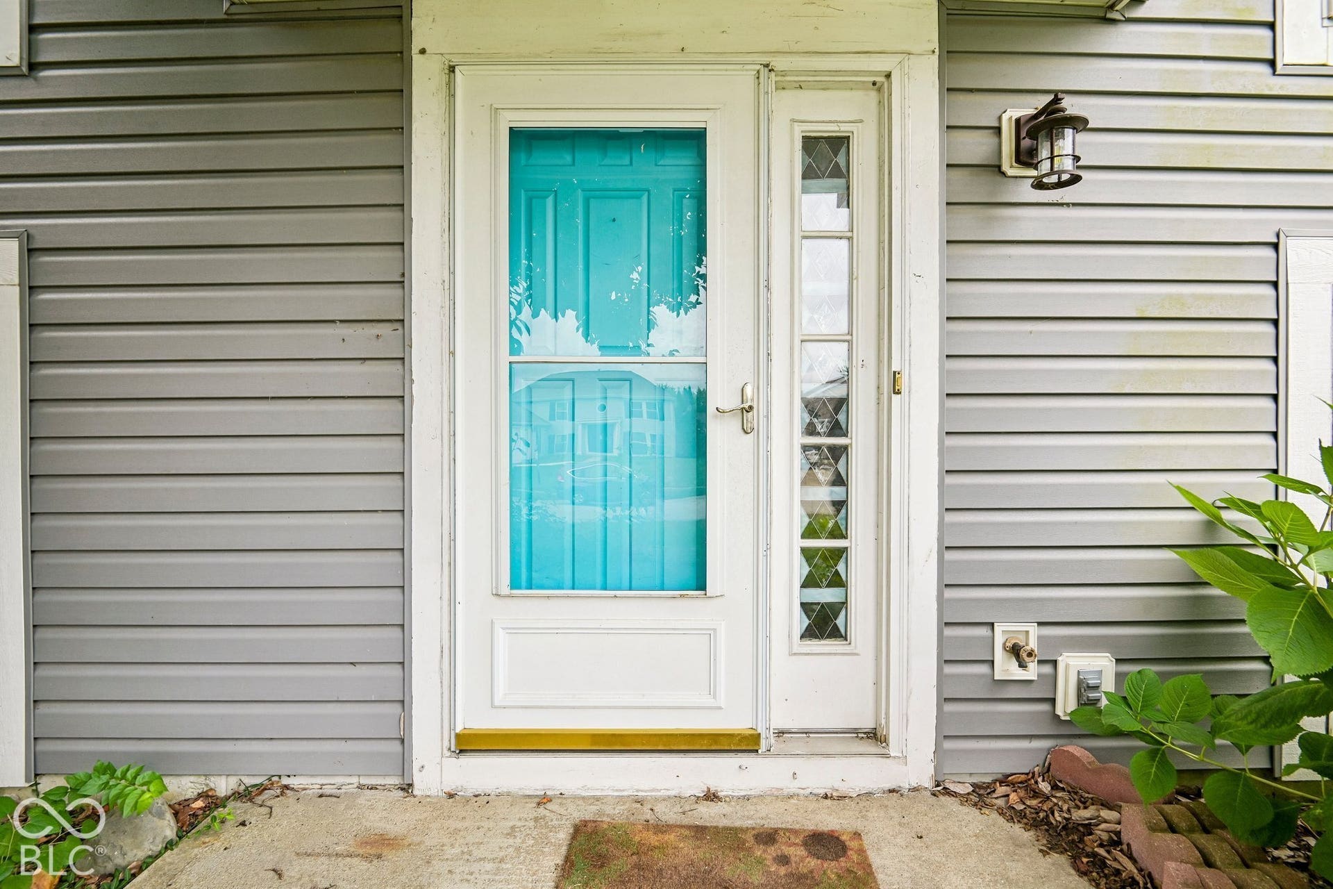 Gray horizontal siding exterior with a white storm door and a teal main door