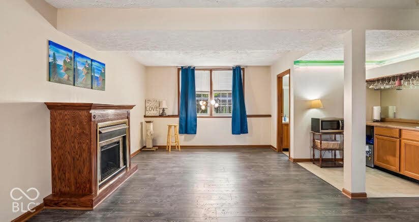 Wood-finish flooring throughout, a gas fireplace with a wood-stained mantel, and a built-in wet bar featuring wood cabinetry, a sink, and glass storage