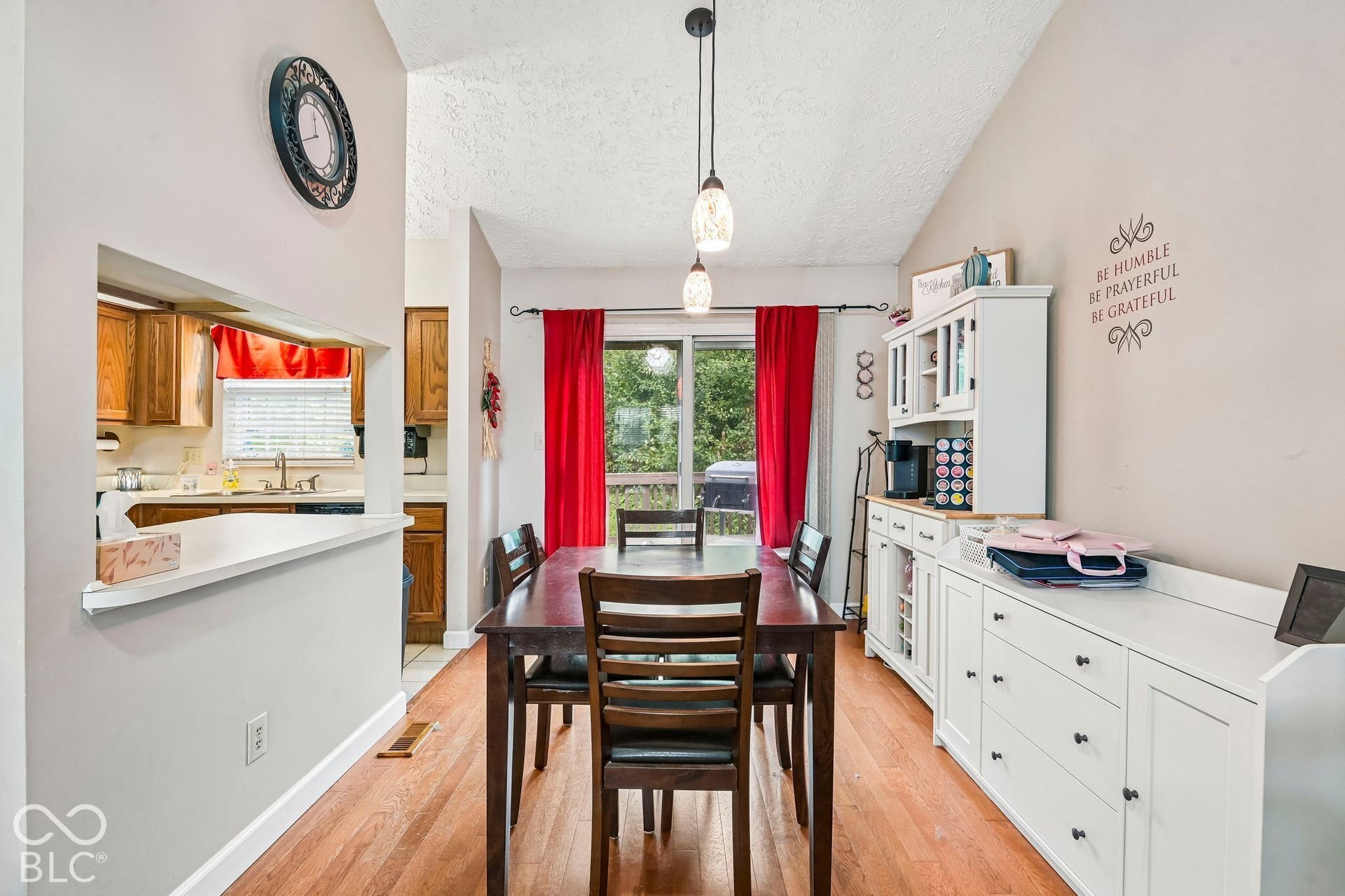 Vaulted ceiling, wood-finish flooring, two pendant light fixtures, pass-through counter, and built-in cabinetry