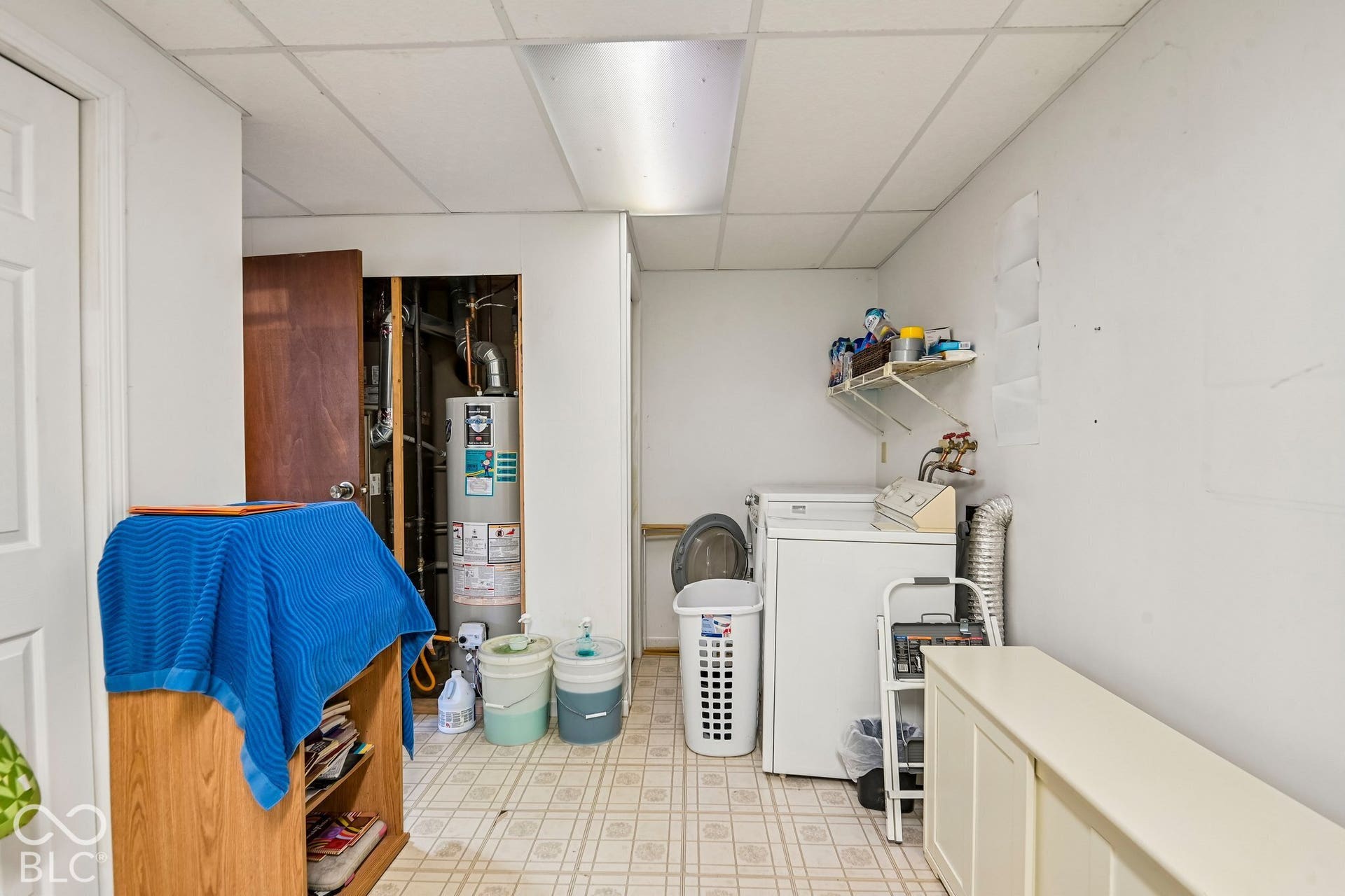 Utility room with patterned flooring, suspended ceiling, and water heater