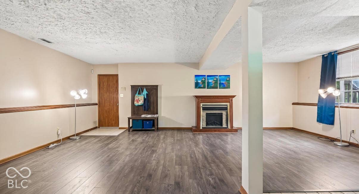 Wood-finish flooring throughout, featuring a fireplace with a wood mantel, a window with a blue curtain, and a paneled door
