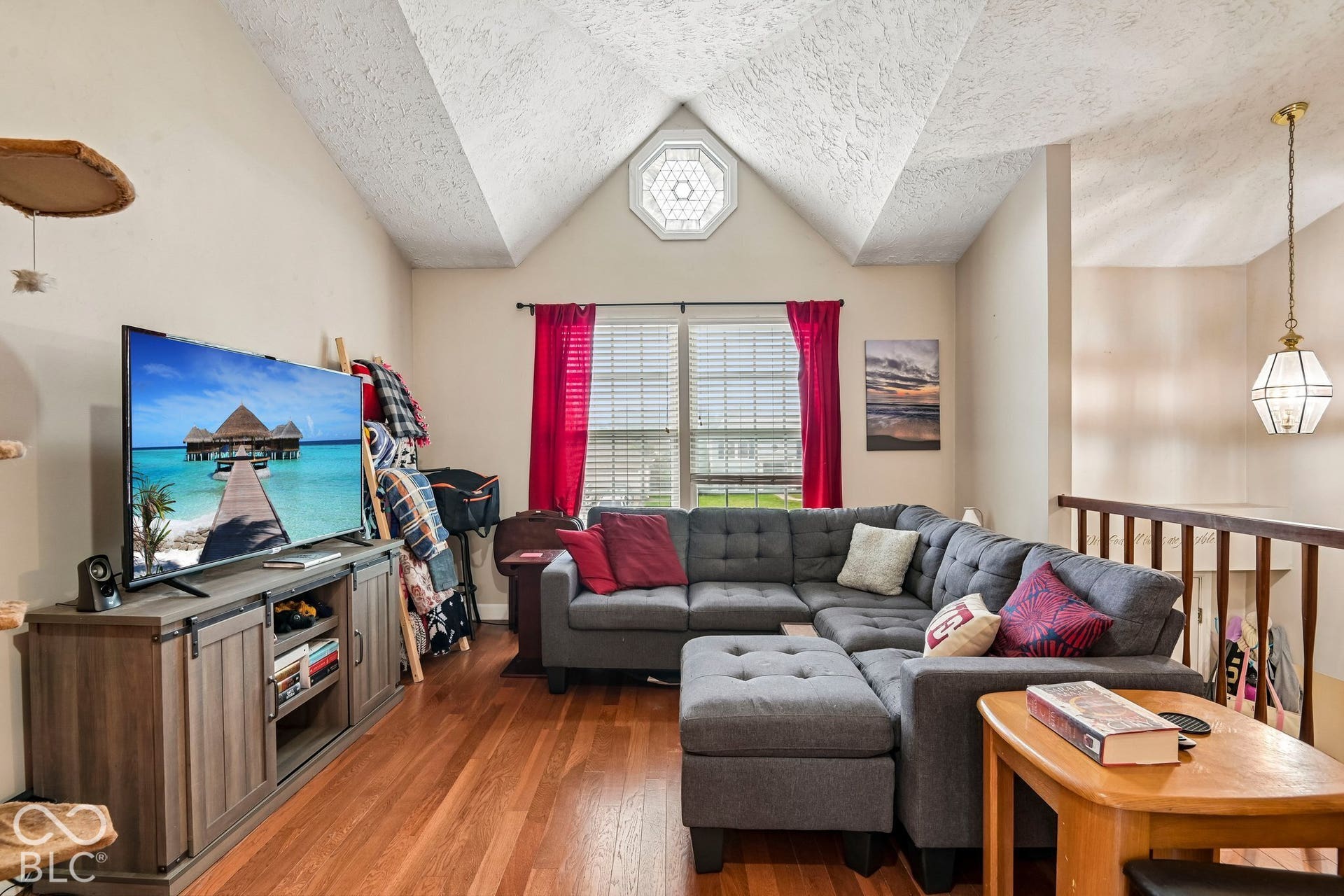 Vaulted ceiling with an octagonal window, wood-finish flooring, and a decorative hanging light fixture