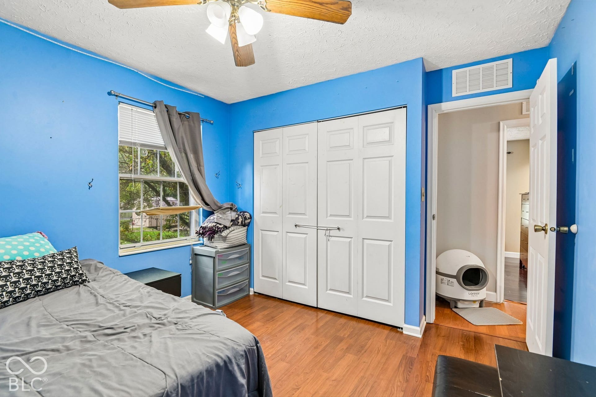 Wood-finish flooring, ceiling fan, window with blinds, and bi-fold closet doors