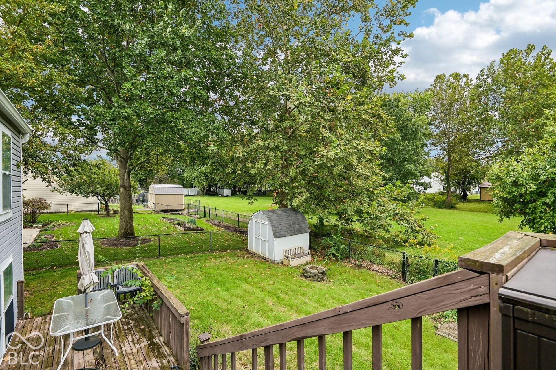 Expansive backyard featuring a manicured lawn, established trees, and two storage sheds