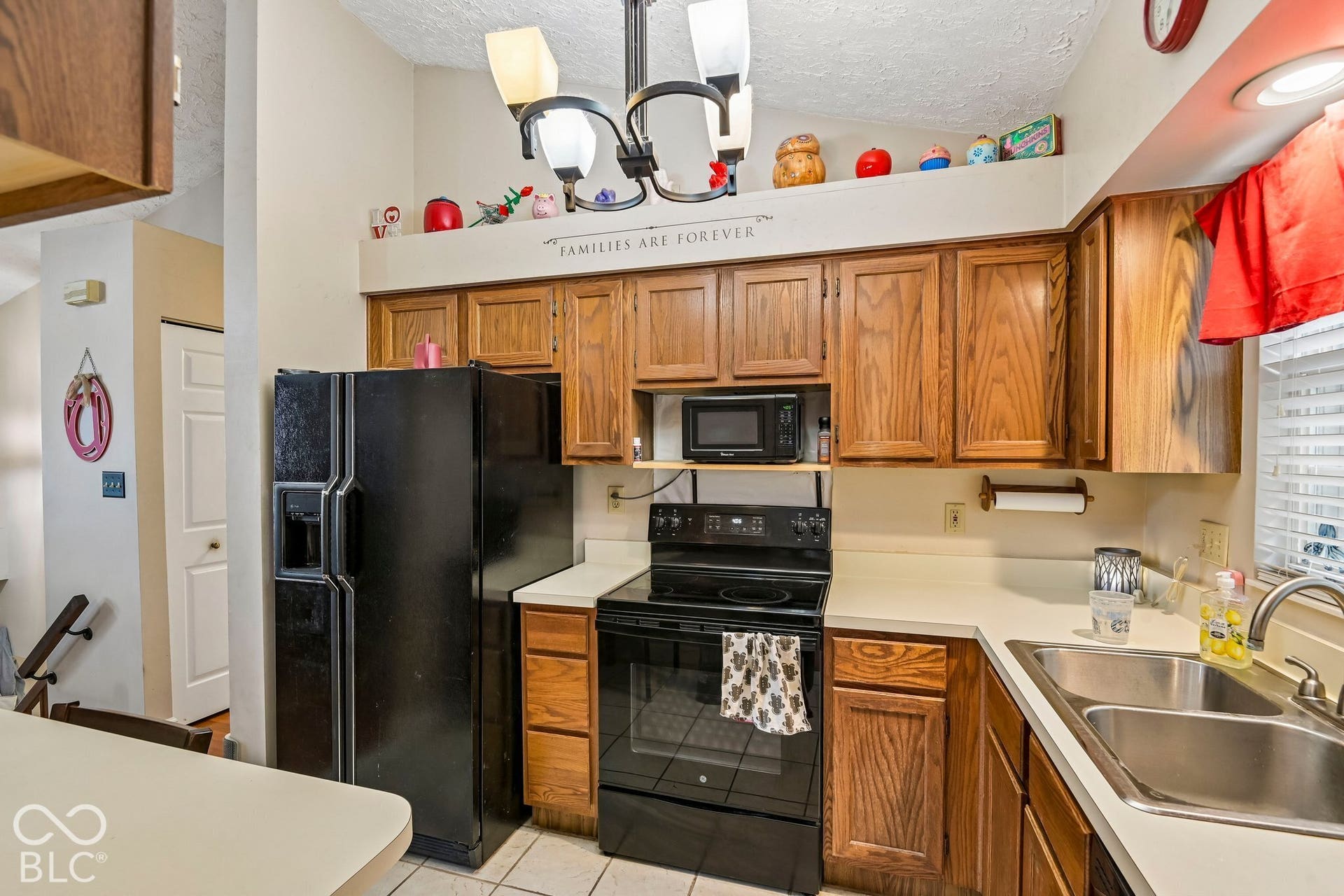 Kitchen featuring wood cabinetry, light-toned countertops, a double basin sink, and black appliances