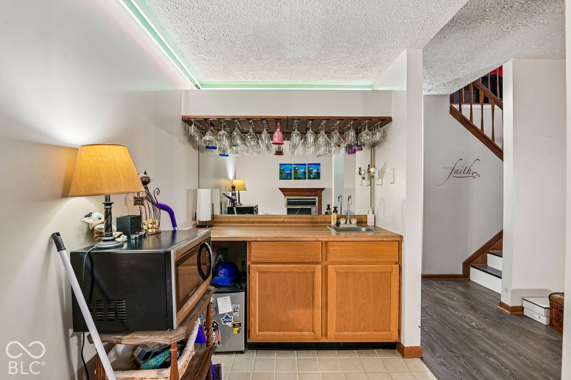 Built-in wet bar with wood-finish cabinetry, stainless steel sink, and glass rack