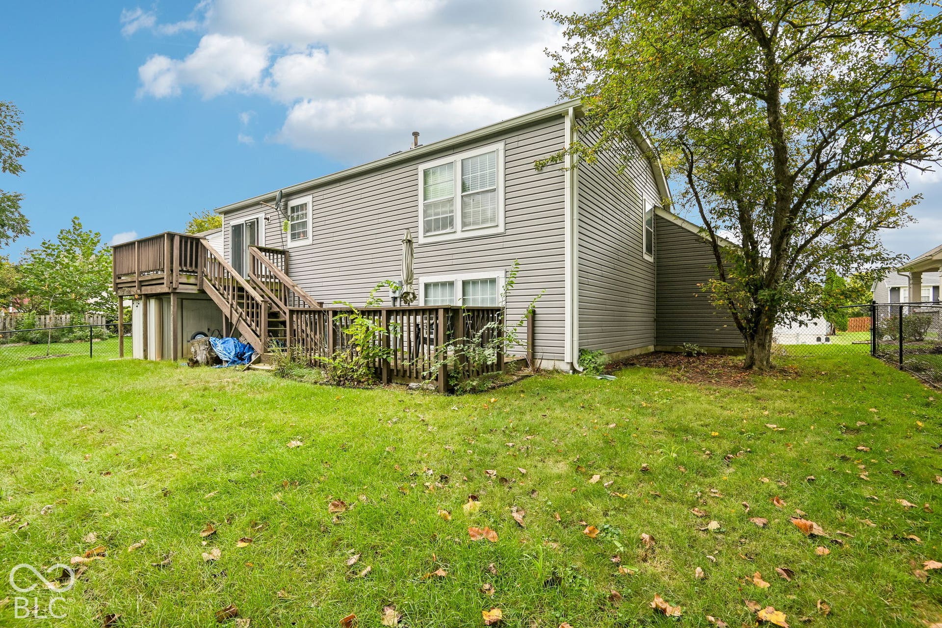 Expansive grassy backyard featuring a multi-level wood deck with stairs, a sliding glass door, and mature trees