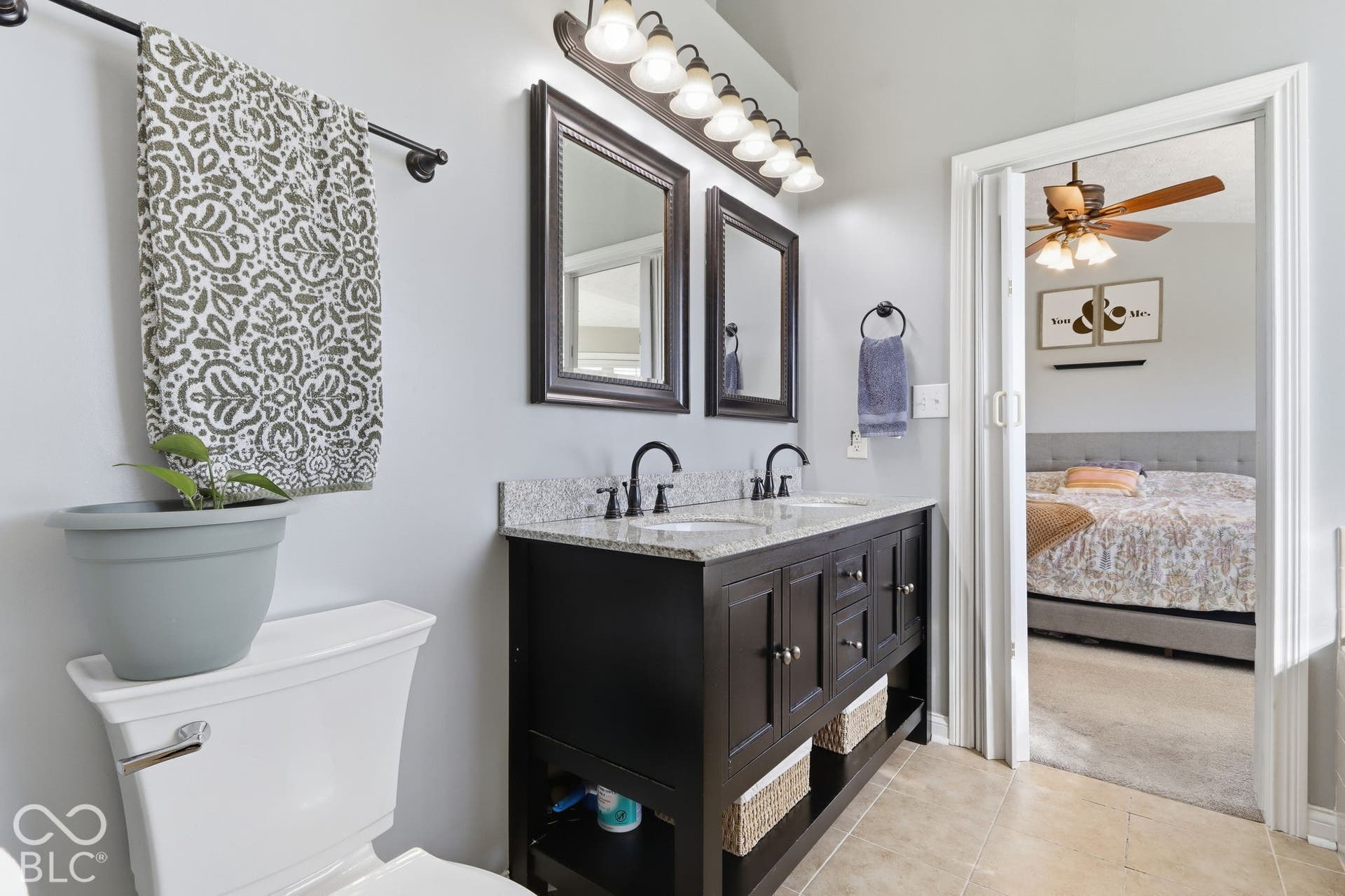 8035 Meadow Bend Lane, Indianapolis, IN 46259 Dual vanity with a stone countertop and integrated sinks, dark wood-finish cabinetry, and framed mirrors, with a white toilet and light-colored tile flooring