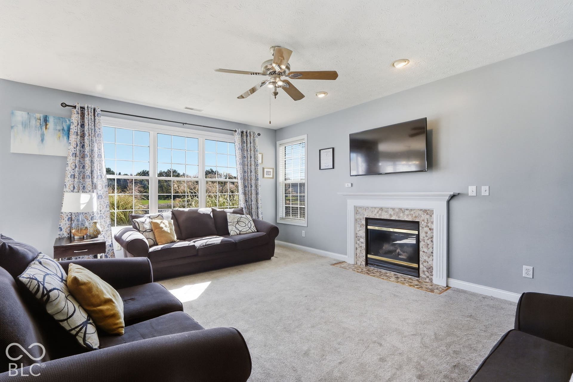 8035 Meadow Bend Lane, Indianapolis, IN 46259 Spacious living area featuring a fireplace with a stone surround, a ceiling fan, recessed lighting, and large multi-pane windows