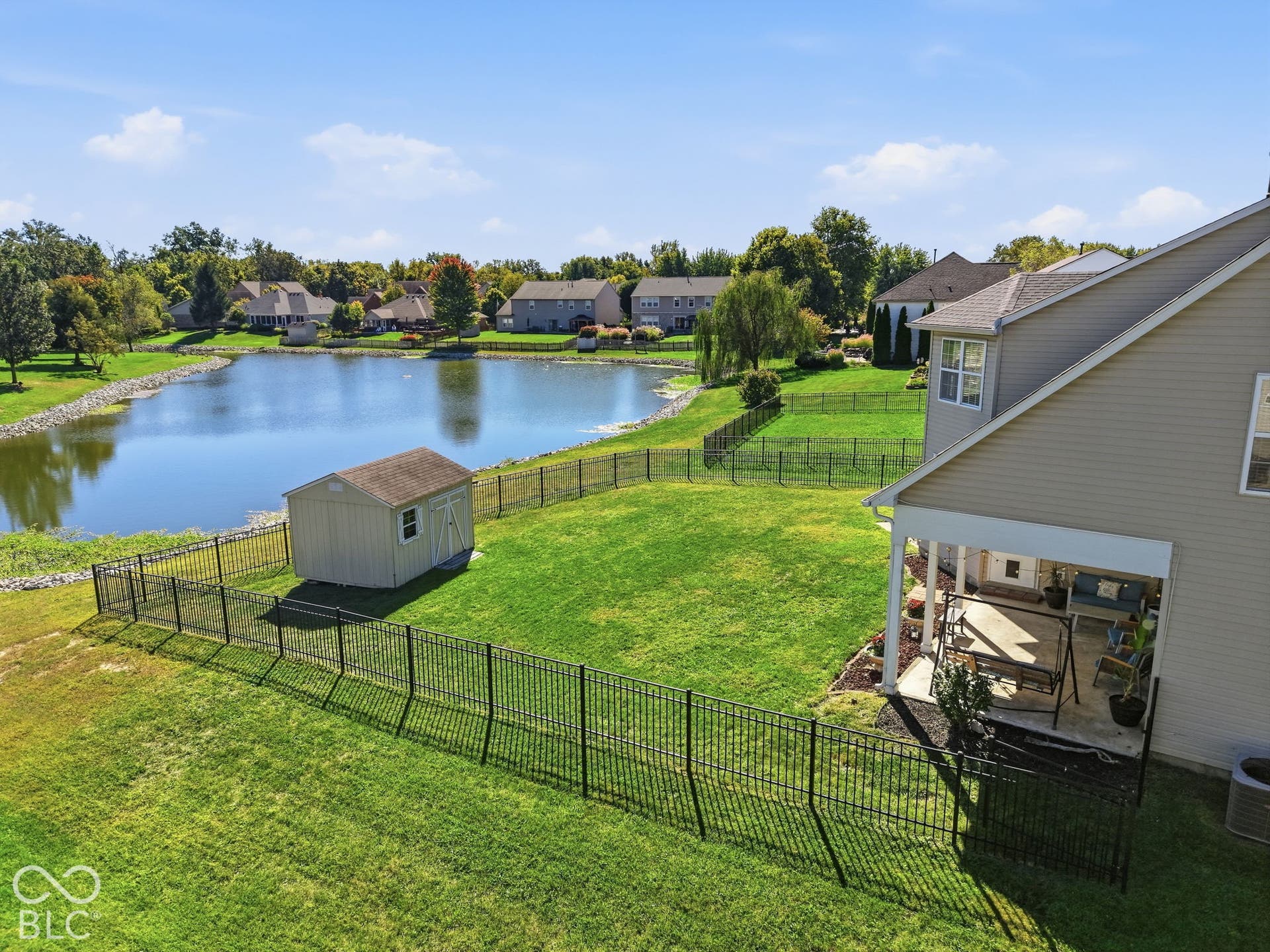 8035 Meadow Bend Lane, Indianapolis, IN 46259 Expansive backyard featuring a manicured lawn, lake frontage, metal fencing, and a storage shed