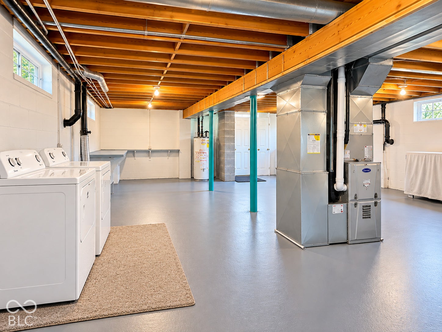 Spacious utility area featuring painted concrete flooring, exposed wood beam ceiling, and a built-in utility sink with shelving