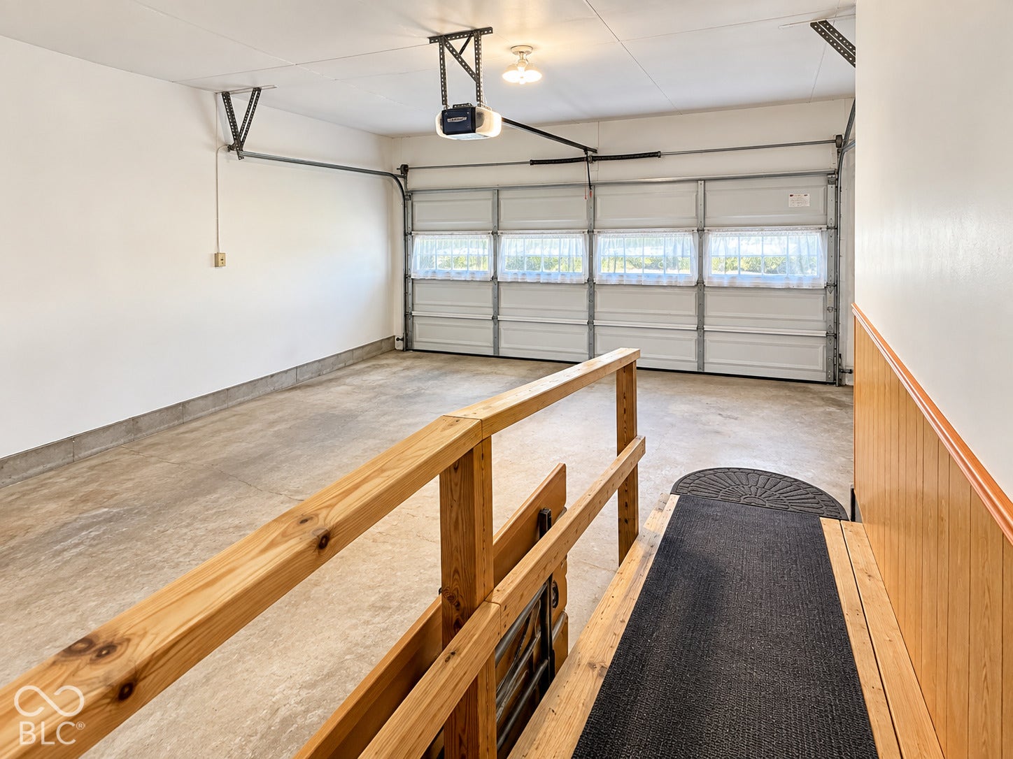 Attached garage with a light-colored concrete floor, white paneling, and an automatic garage door opener
