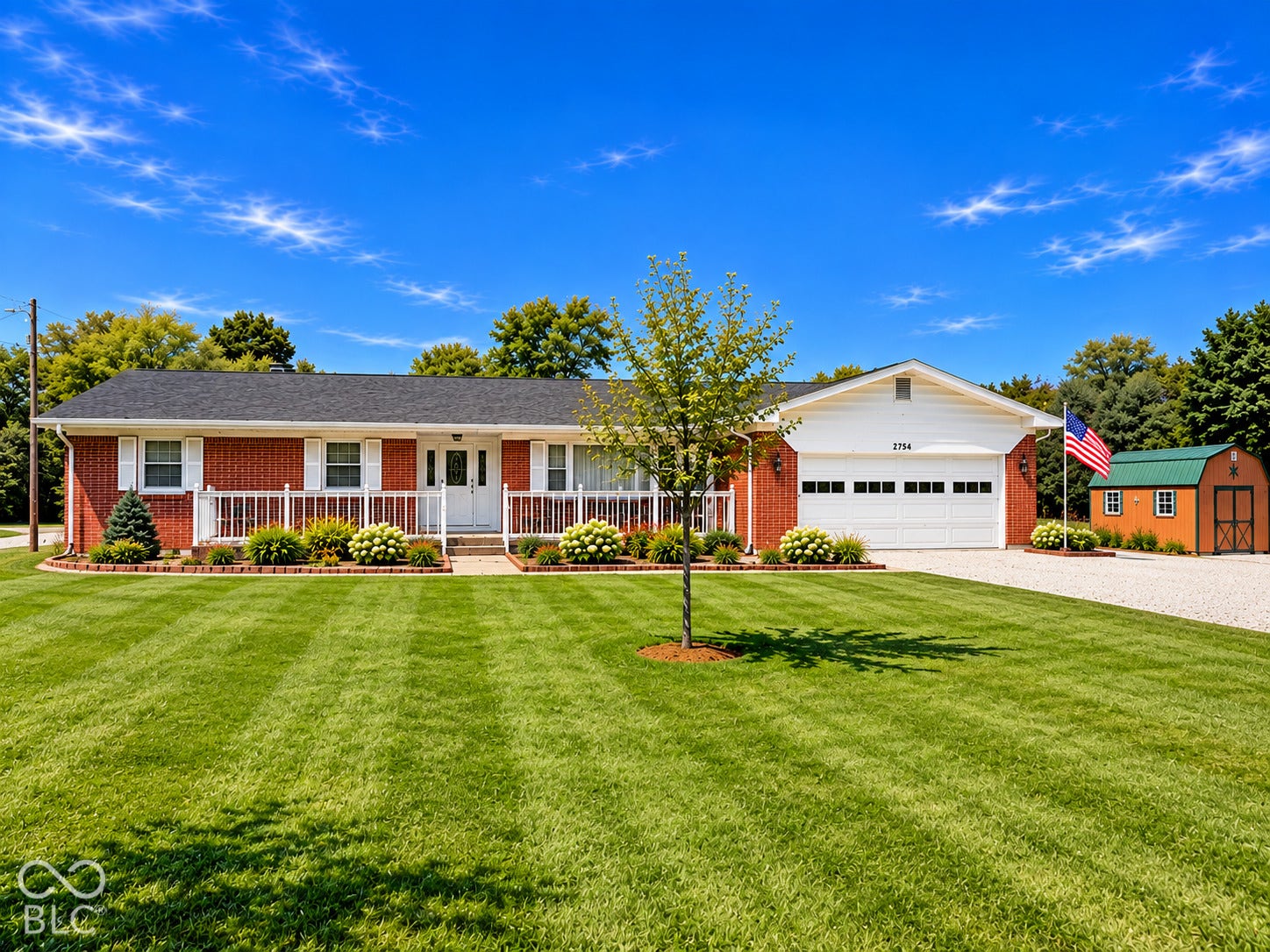 Brick exterior residence with an attached two-car garage, a covered front porch with white railing, and a detached storage shed with a green metal roof