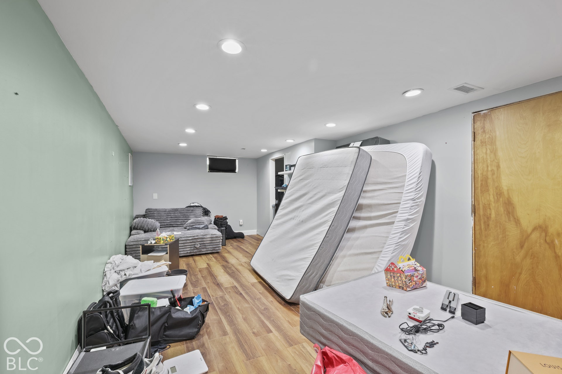 Recessed ceiling lighting, wood-finish flooring, light-colored walls, and a wood panel door