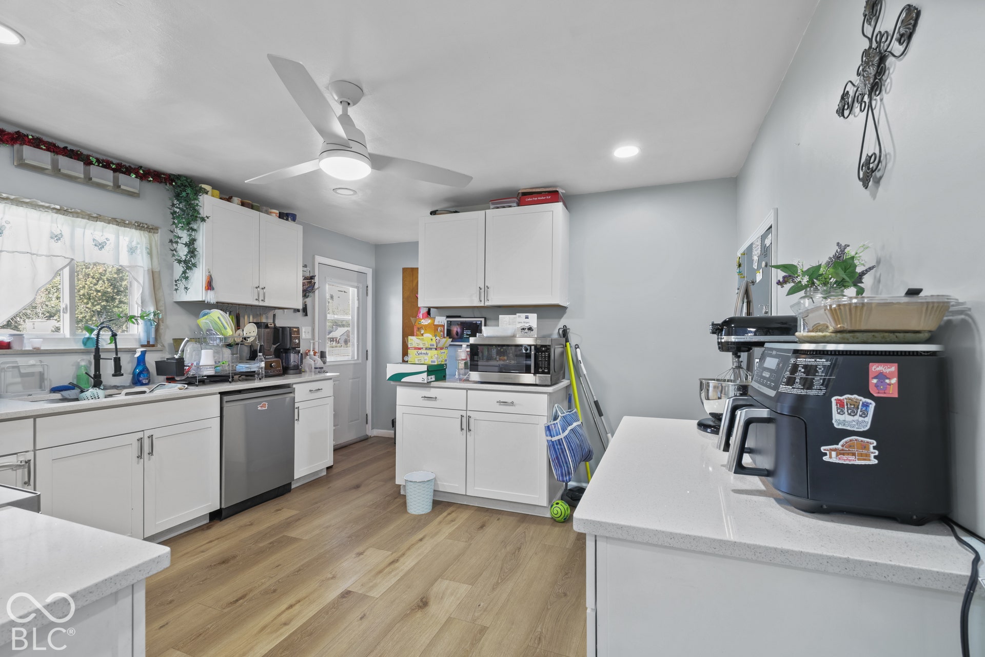 Kitchen featuring wood-finish flooring, white cabinetry, a stainless steel dishwasher, and light-toned countertops