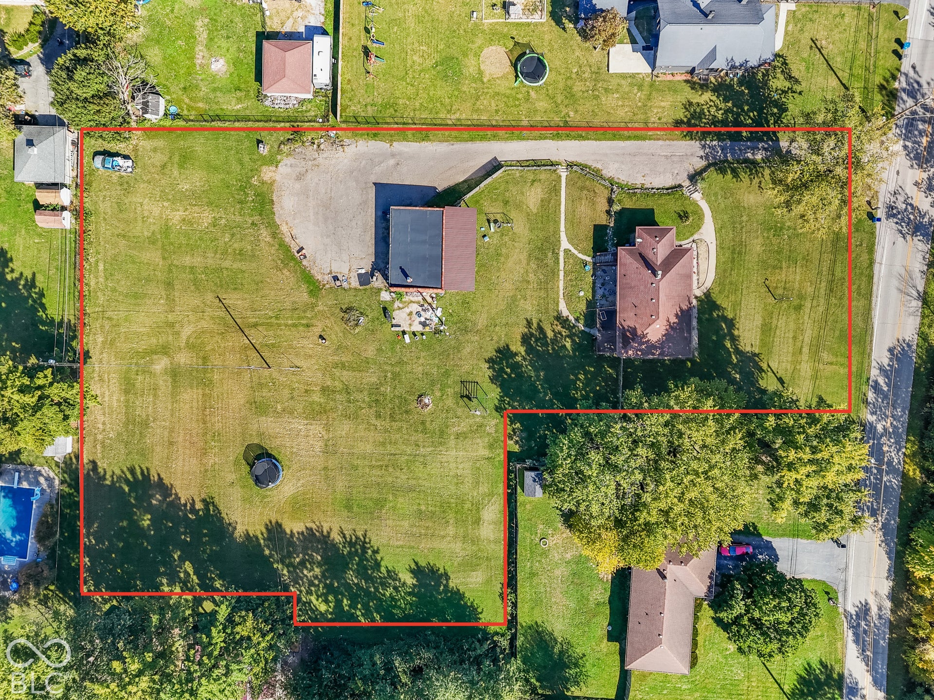 Expansive lot featuring a primary residence with a multi-gabled roof, an auxiliary structure with a dark roof, a gravel parking area, and mature trees