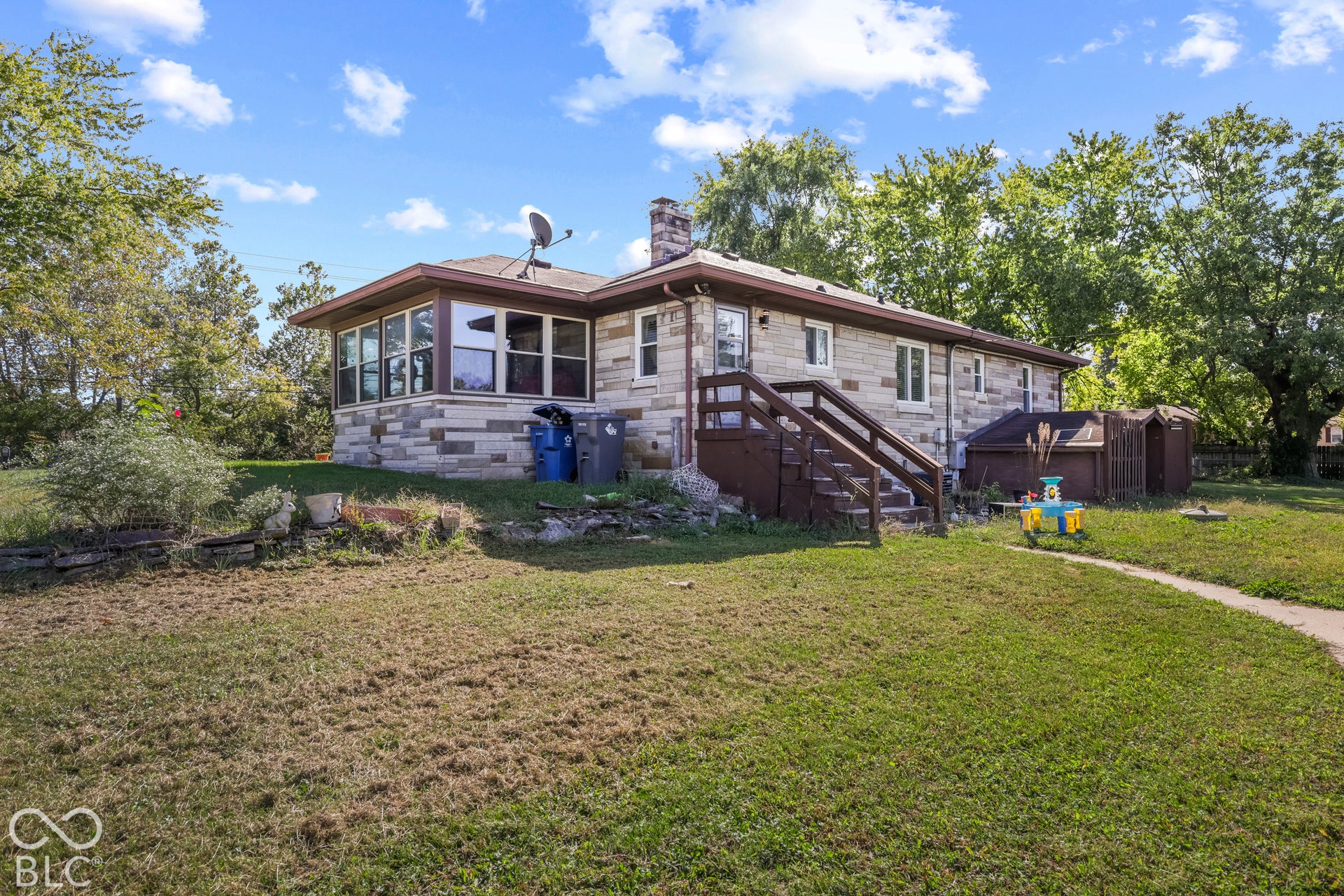 Stone exterior featuring multiple windows, a sunroom extension, a wooden deck, and a chimney