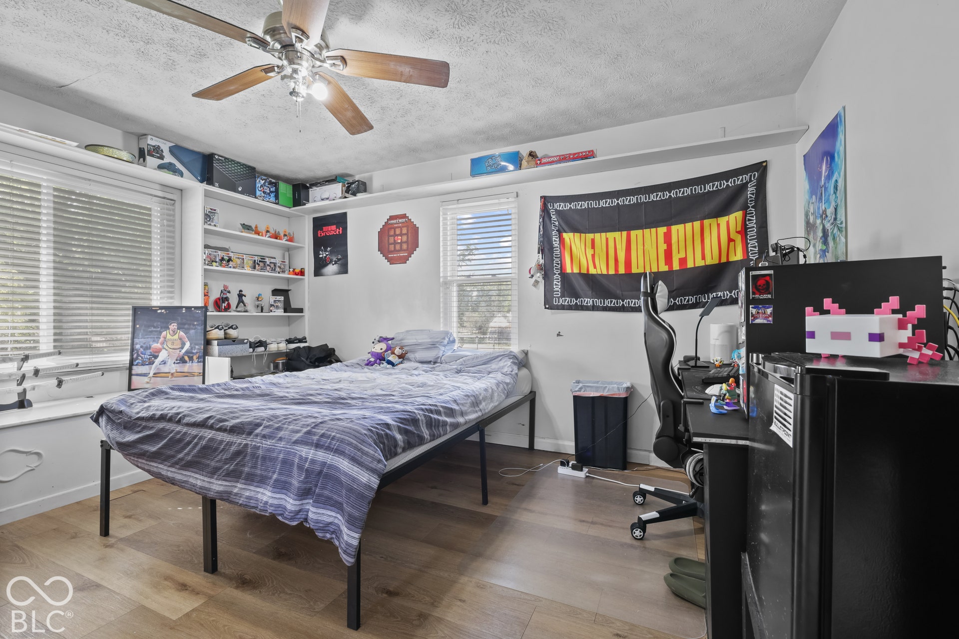 Wood-finish flooring, two windows with blinds, built-in shelving, and a ceiling fan with light fixture